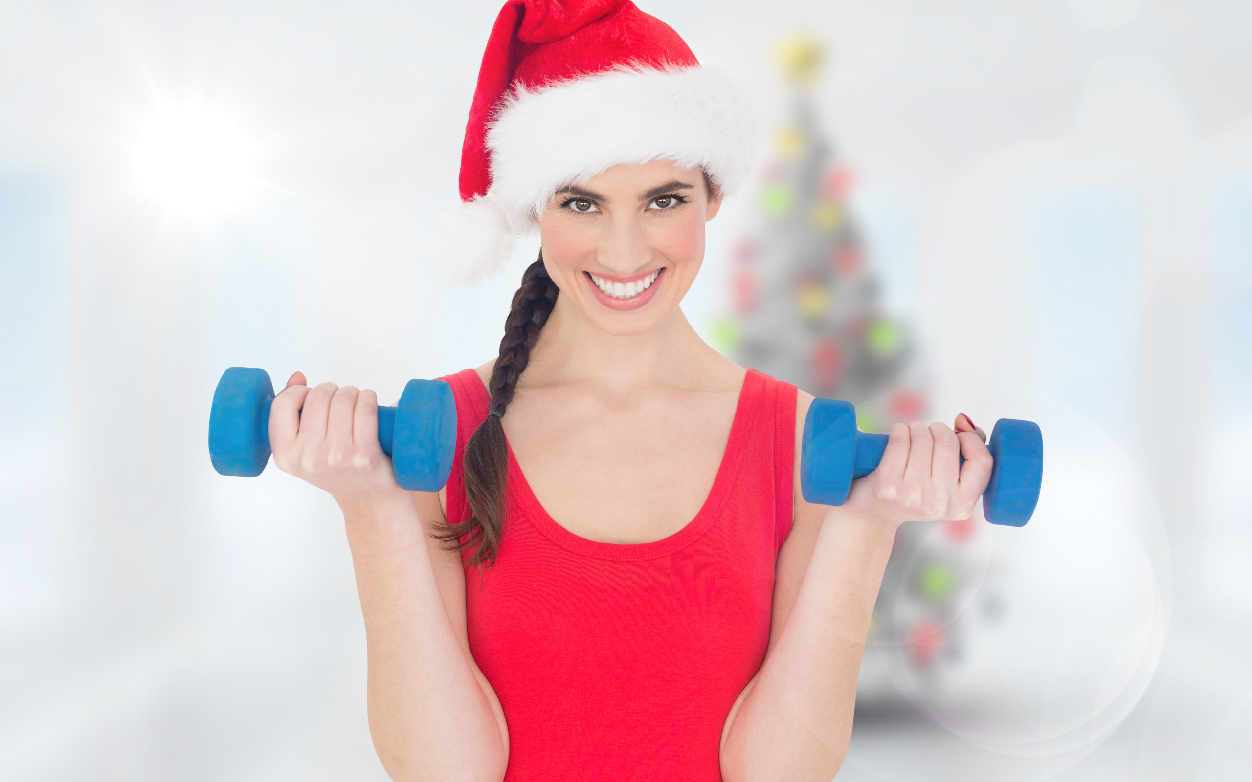 Красивая девушка в шапке Санта Клауса с гантелями в руках 