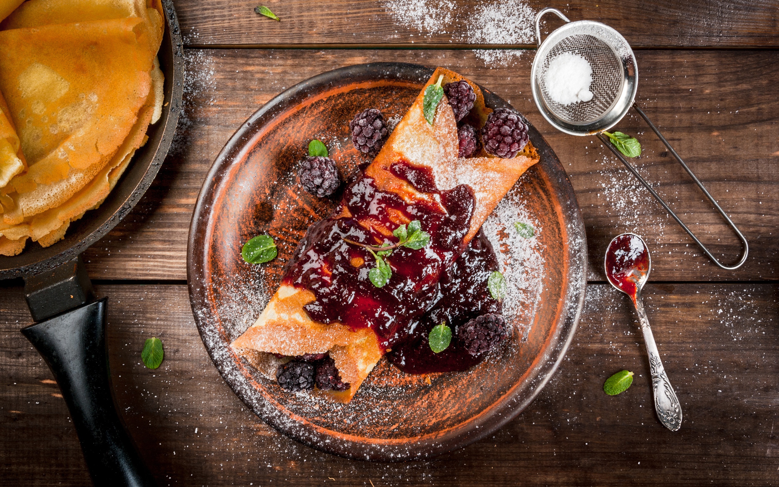 Блин с ягодами и джемом на тарелке с сахарной пудрой