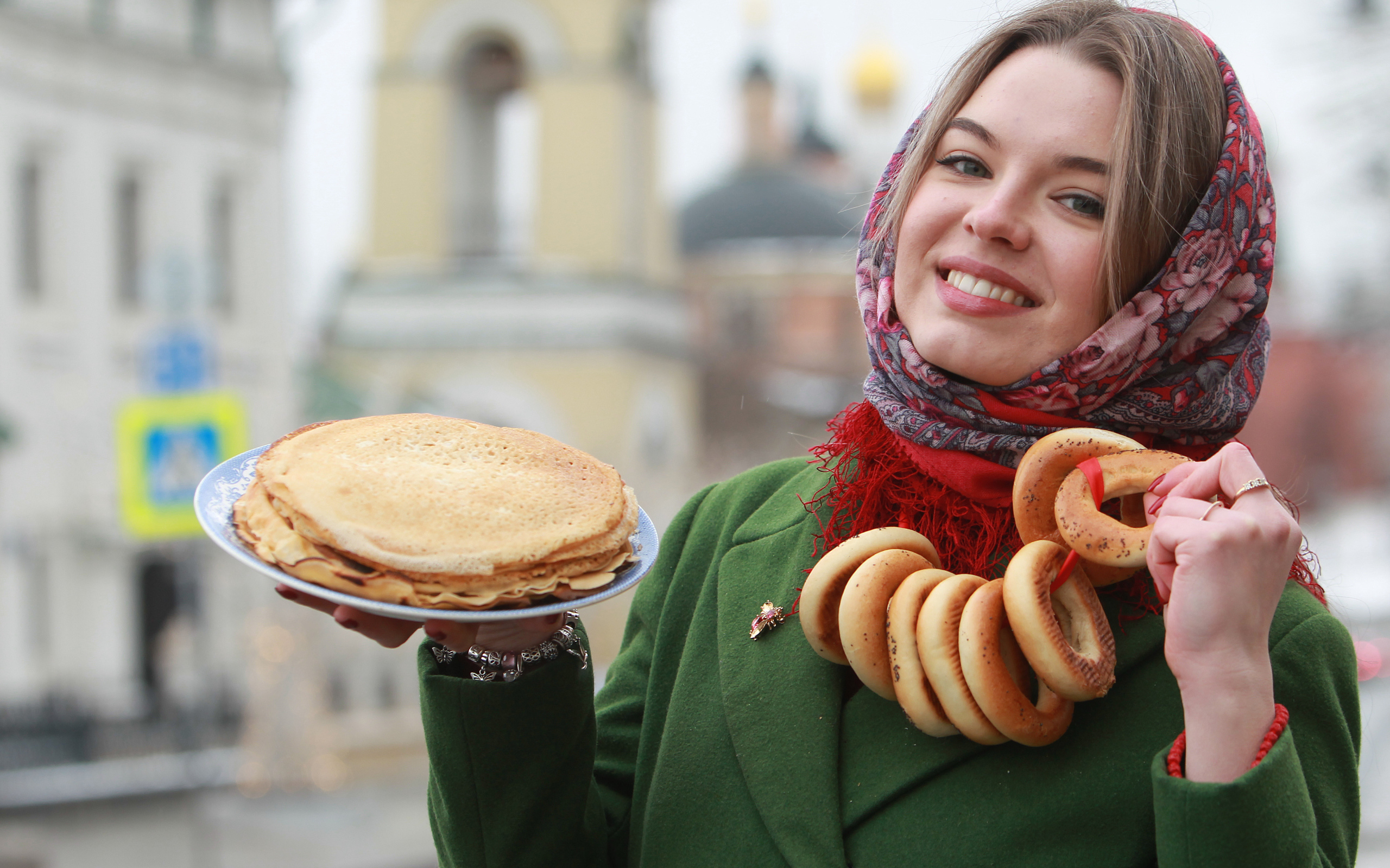 Улыбающаяся девушка с блинами и баранками на Масленицу