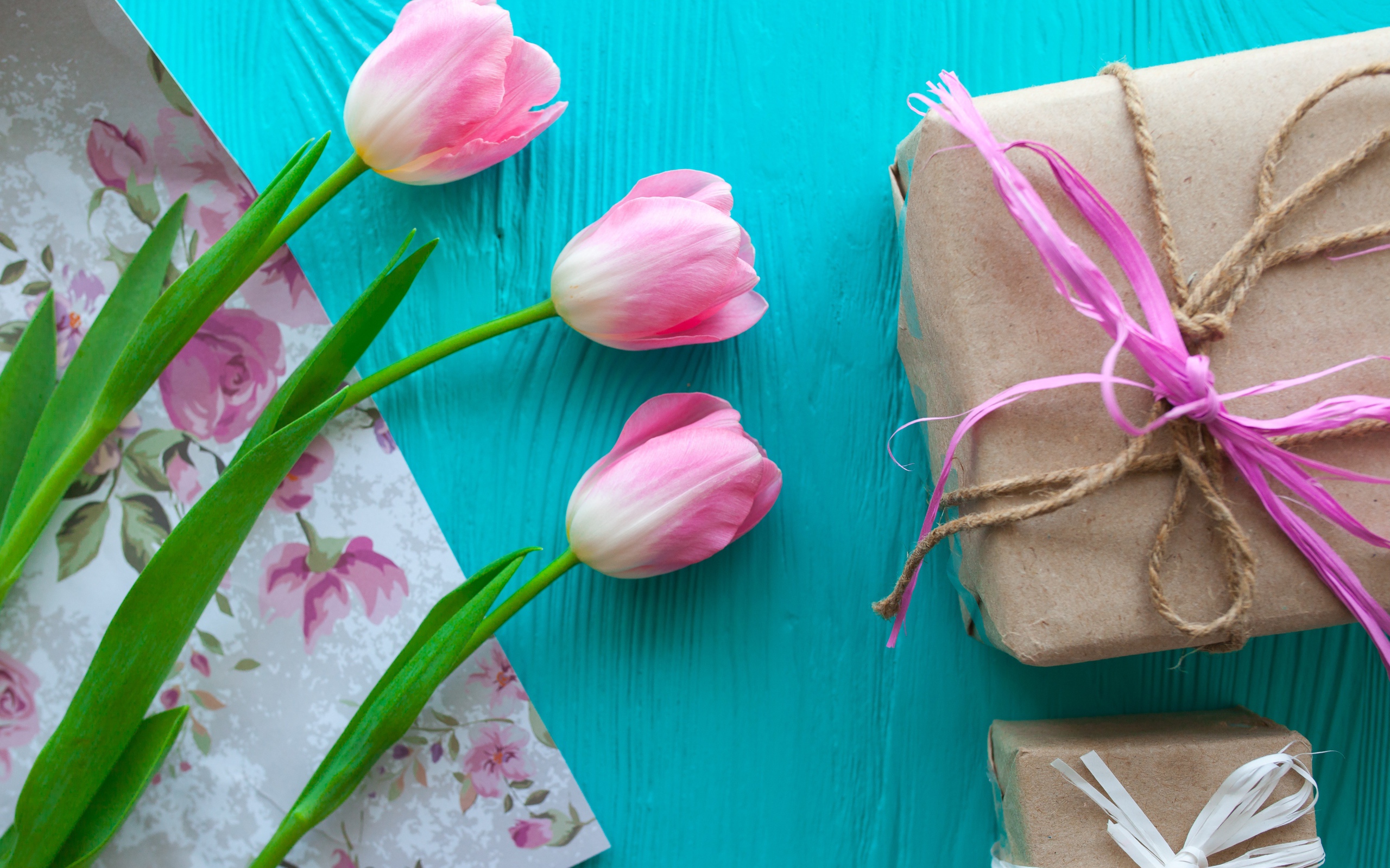 Три розовых тюльпана на голубом столе с подарками