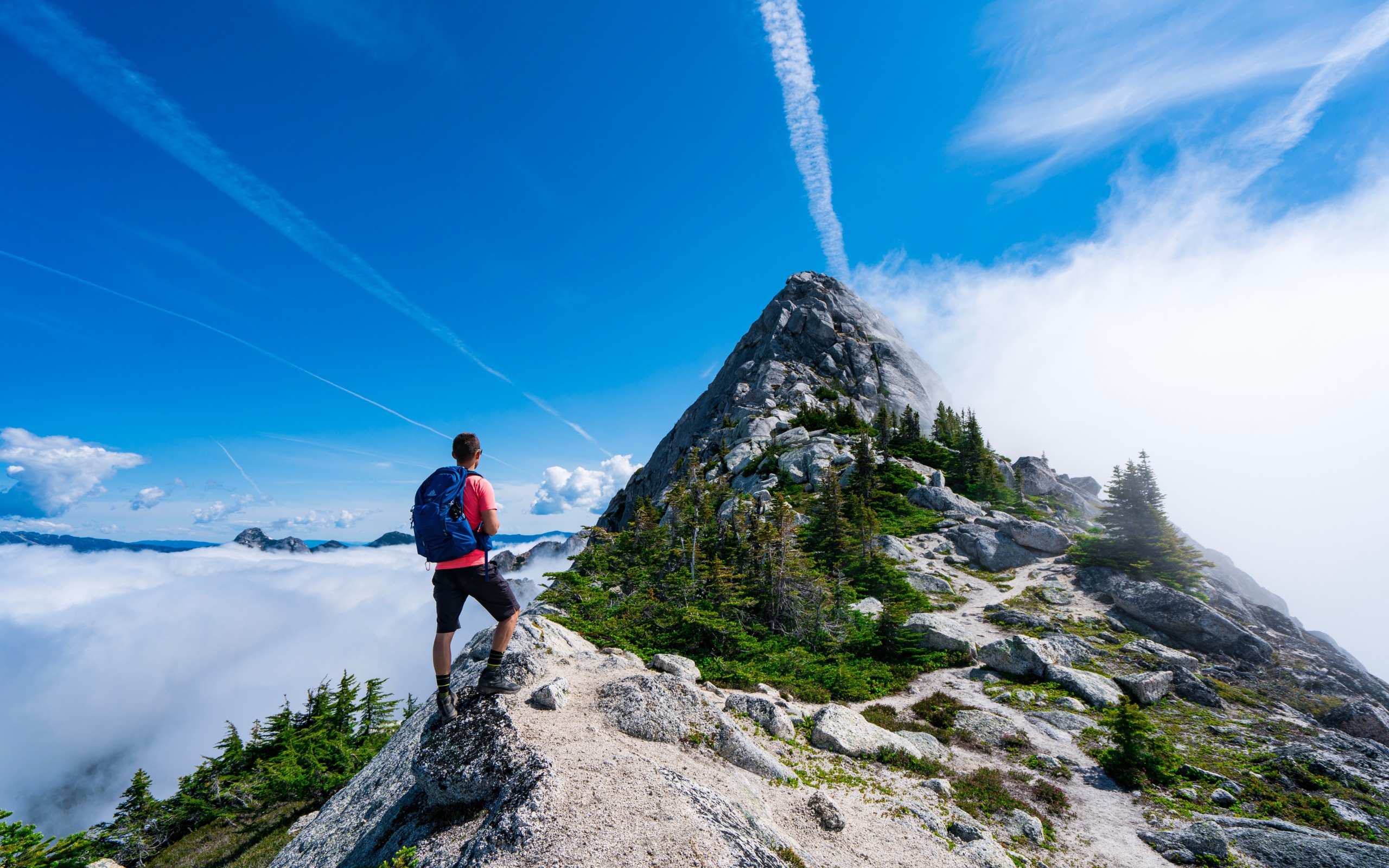Мужчина подымается на вершина горы под голубым небом 