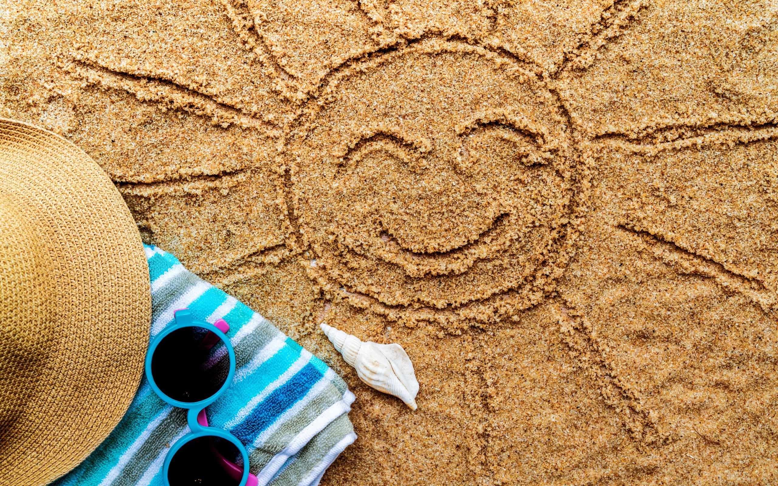 Нарисованное на песке солнце со шляпой и очками летом