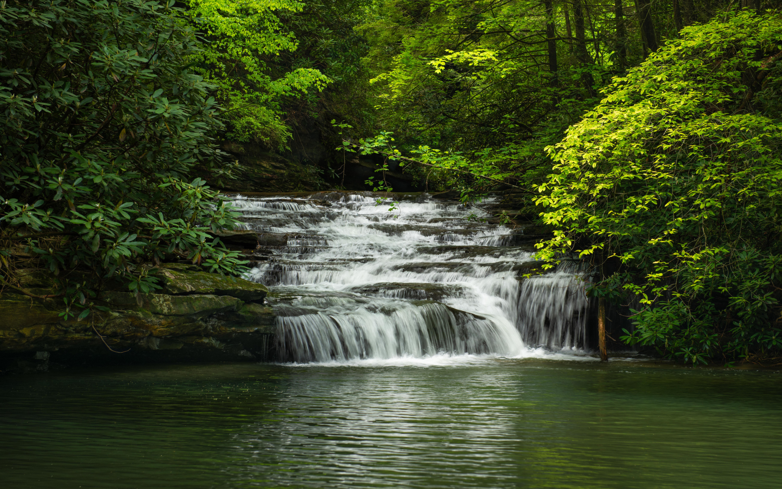 Водопад стекает по каменному каскаду в реку 