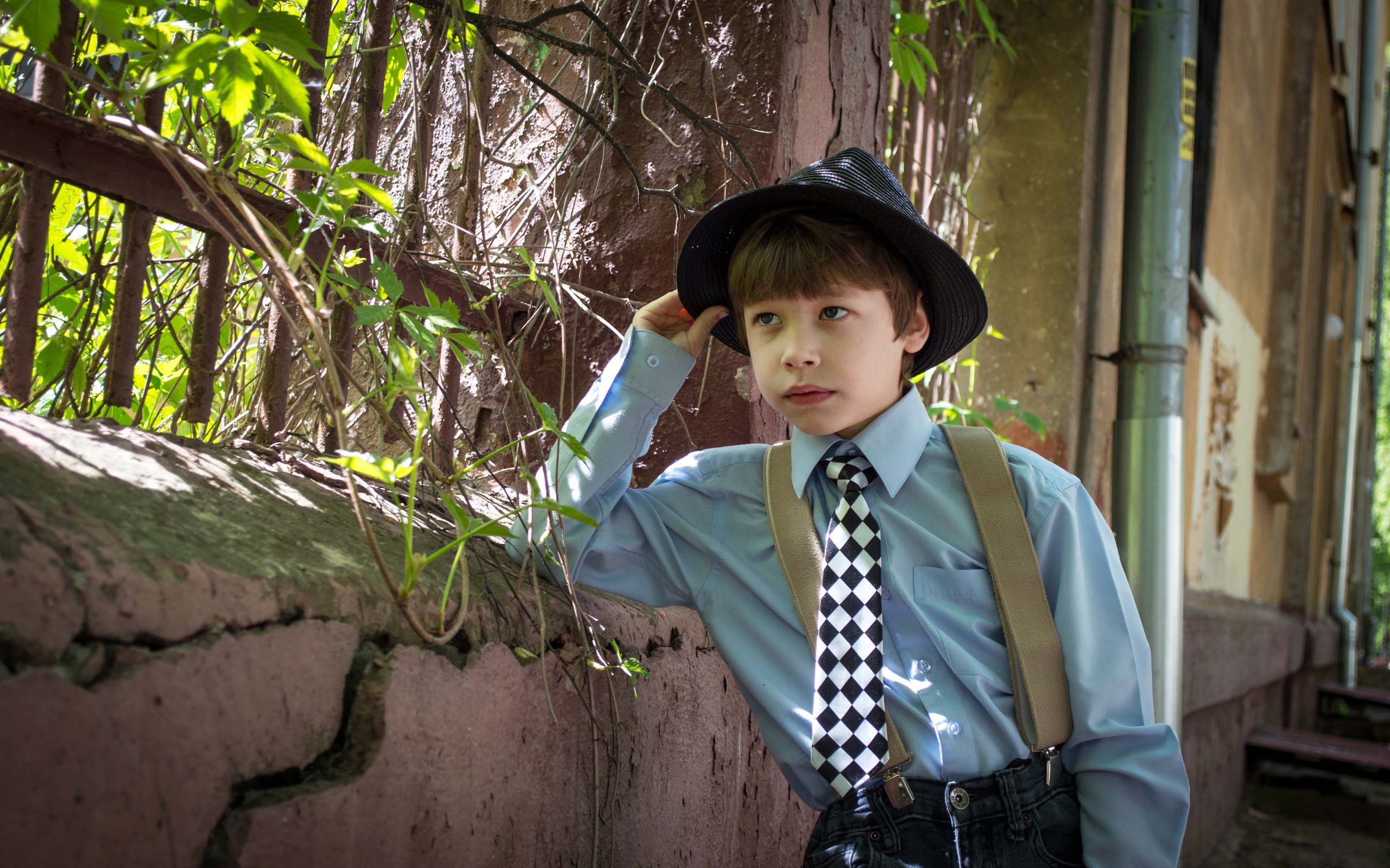 Красивый мальчик в шляпе стоит у забора 