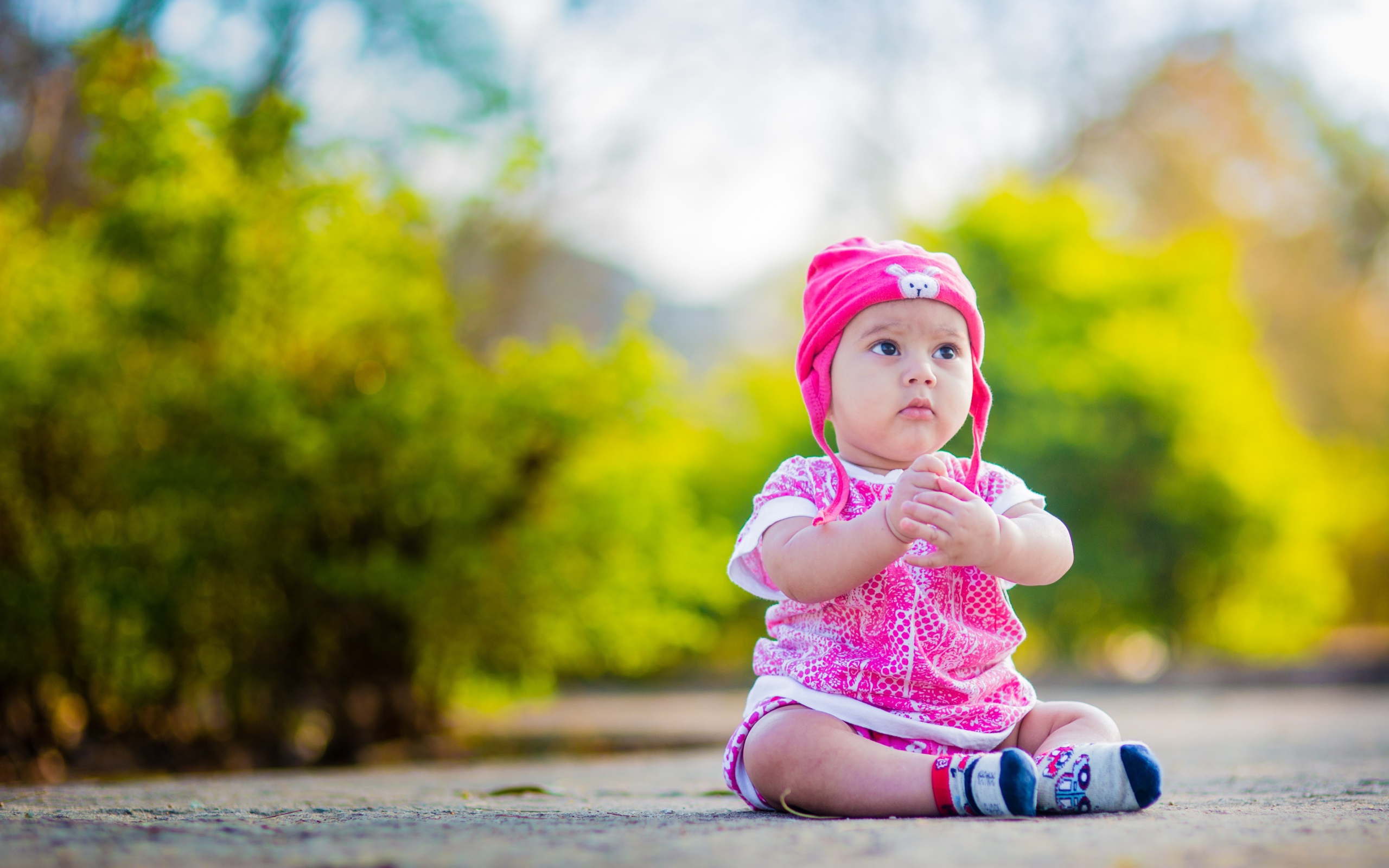Маленькая девочка в розовом костюме сидит на земле