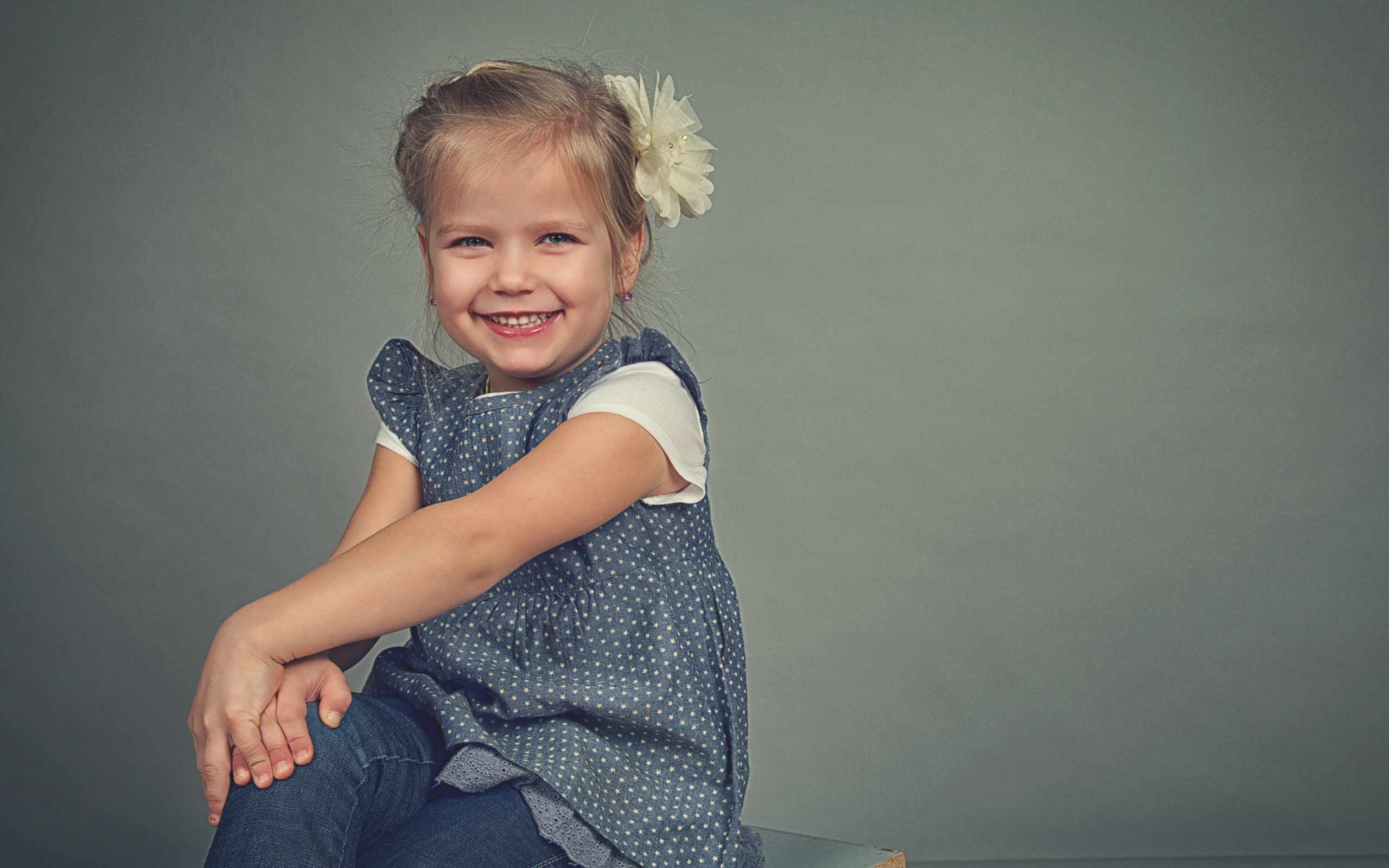 Маленькая улыбающаяся девочка с бантом на сером фоне 