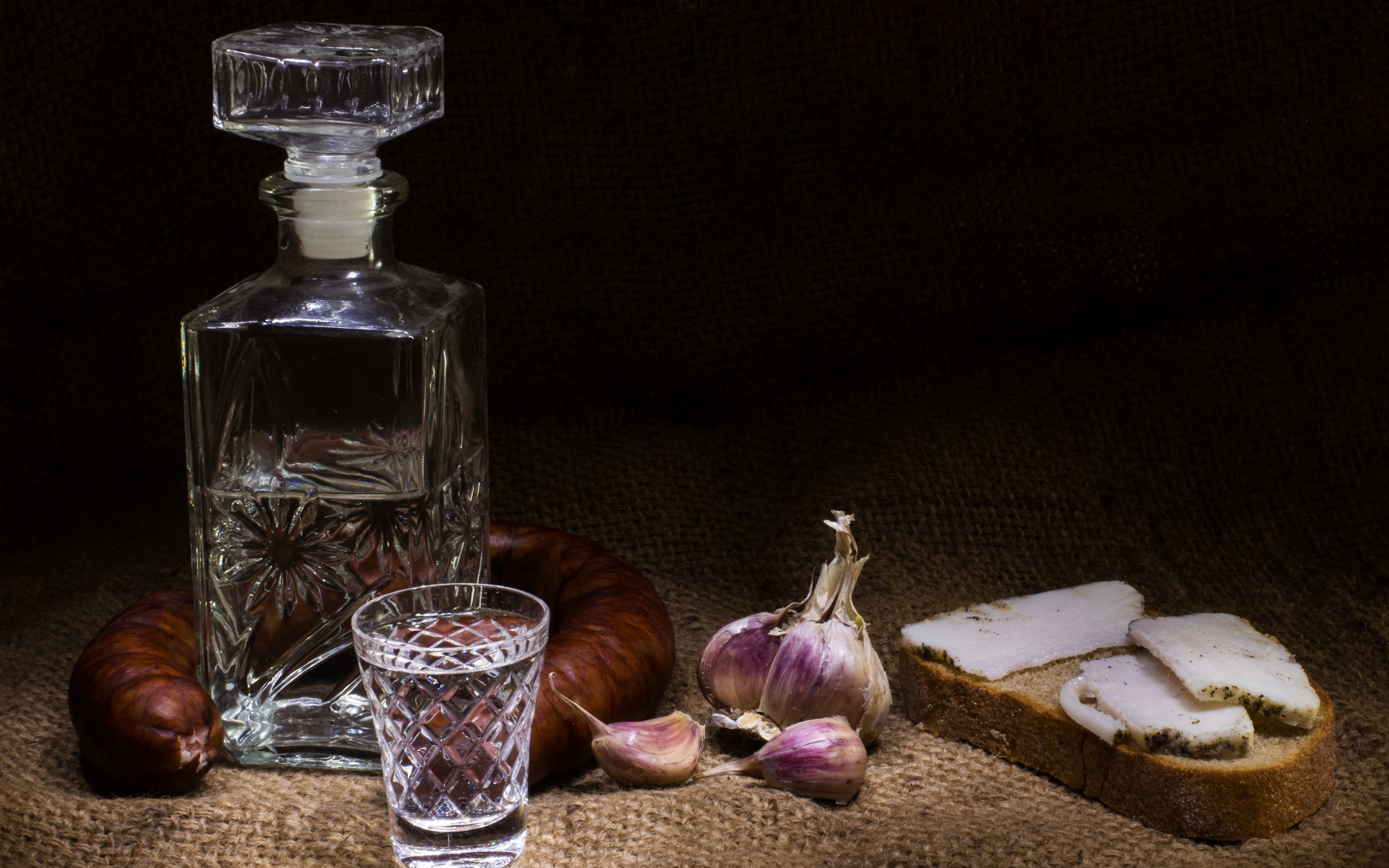 Бутылка водки на столе с салом, колбасой и чесноком