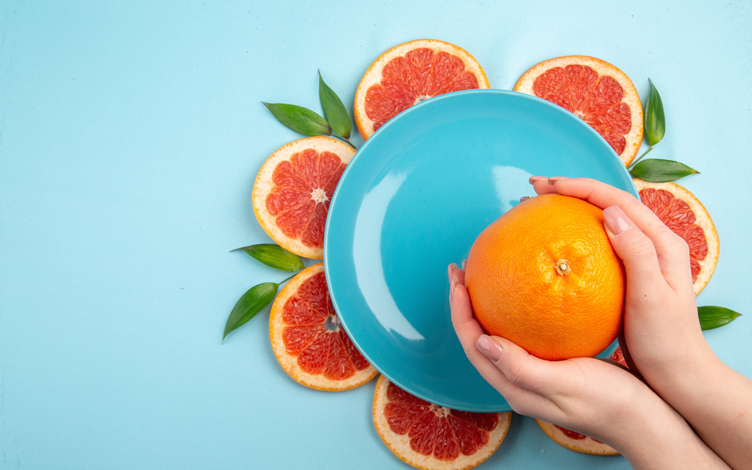 Апельсин в руках девушки на голубом фоне с тарелкой