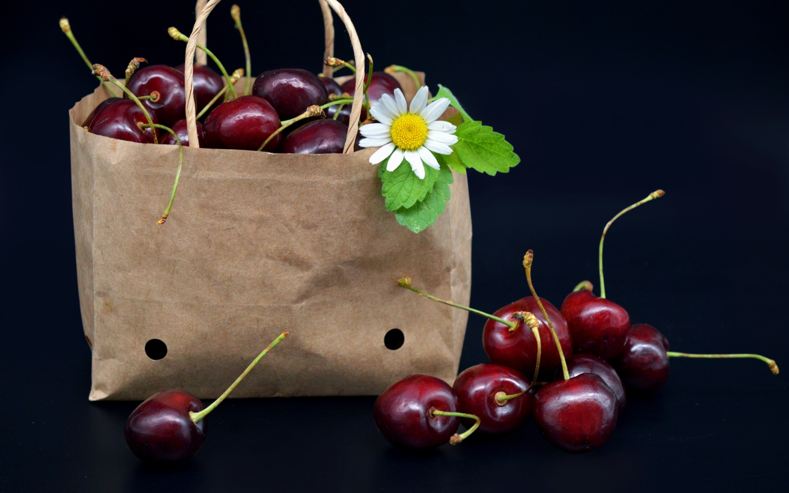 Бумажный пакет с ягодами черешни на черном фоне