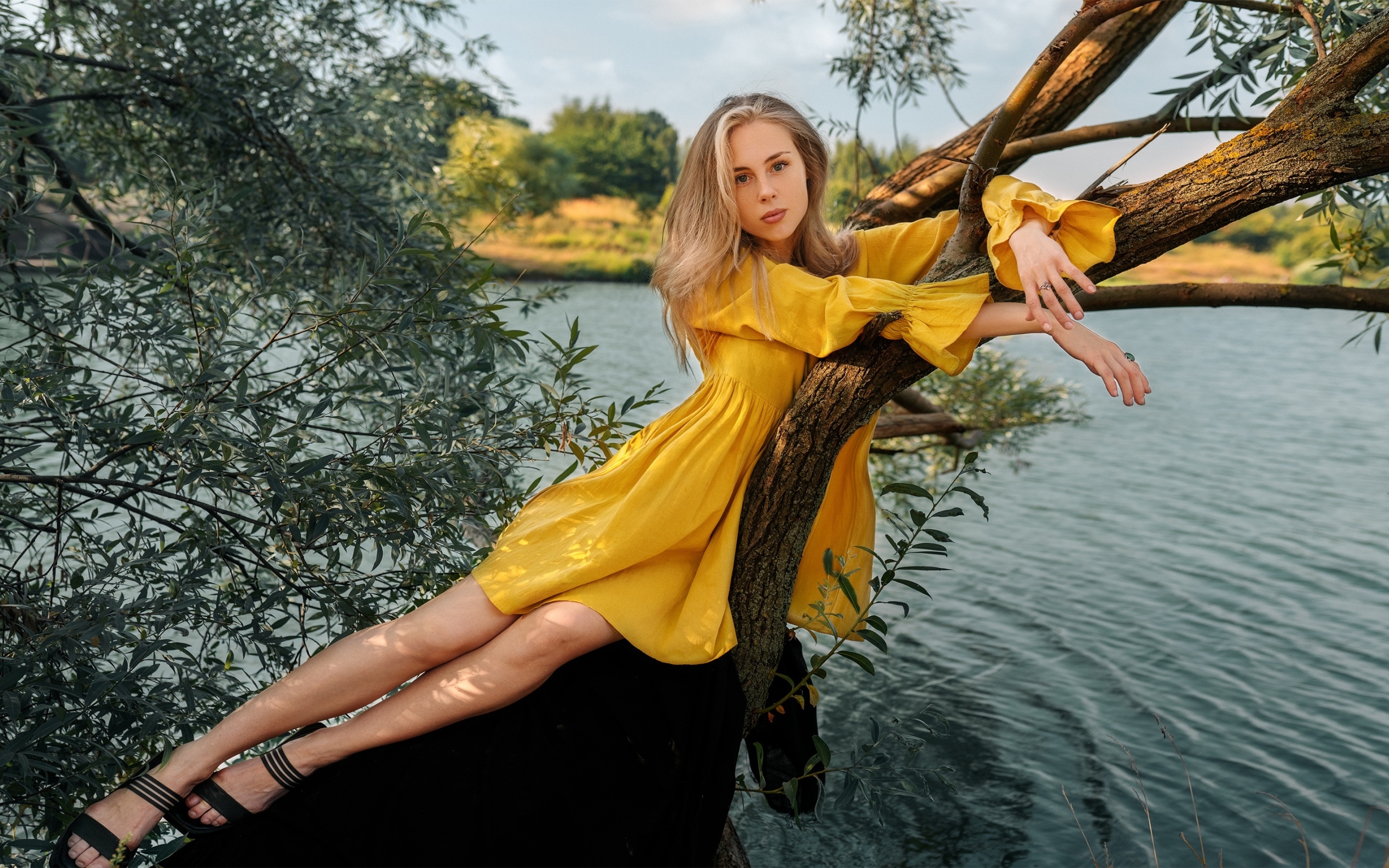 Красивая девушка в желтом платье лежит на дереве у воды