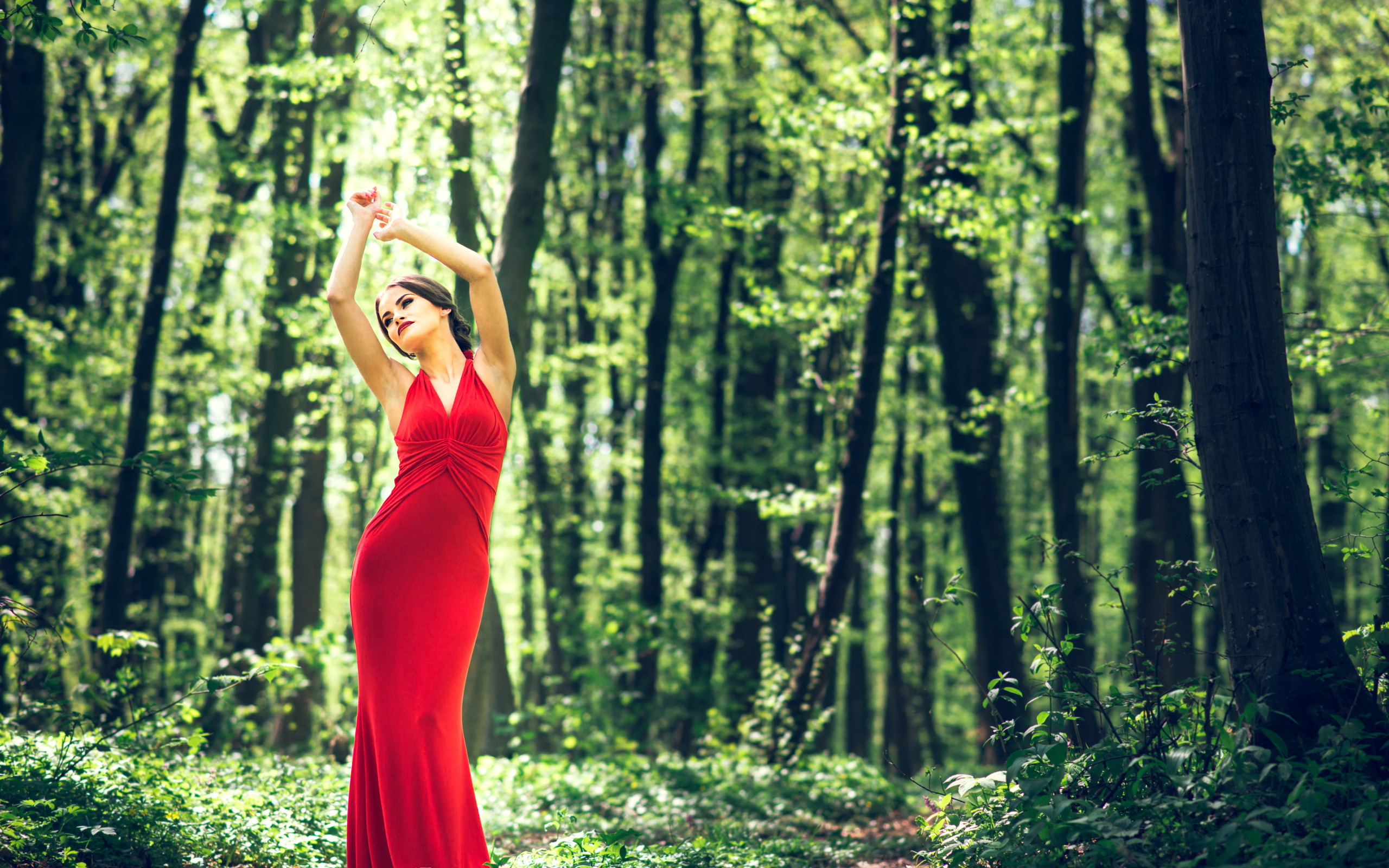 Девушка в красивом красном платье стоит в лесу