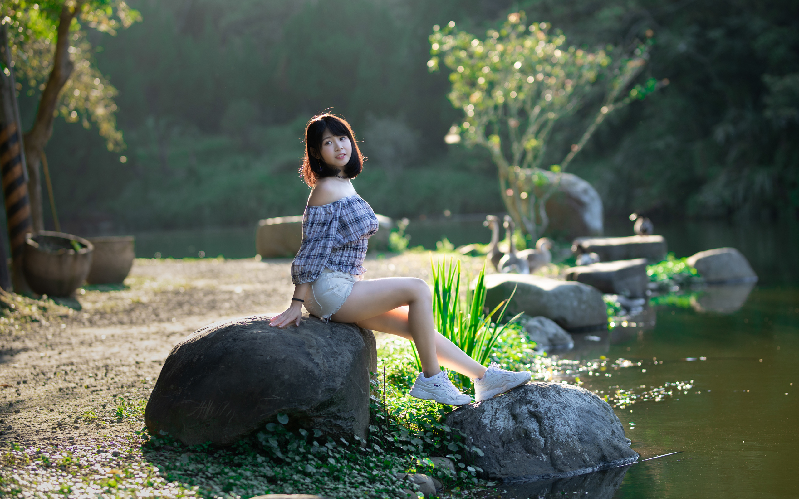 Девушка сидит на большом камне у пруда