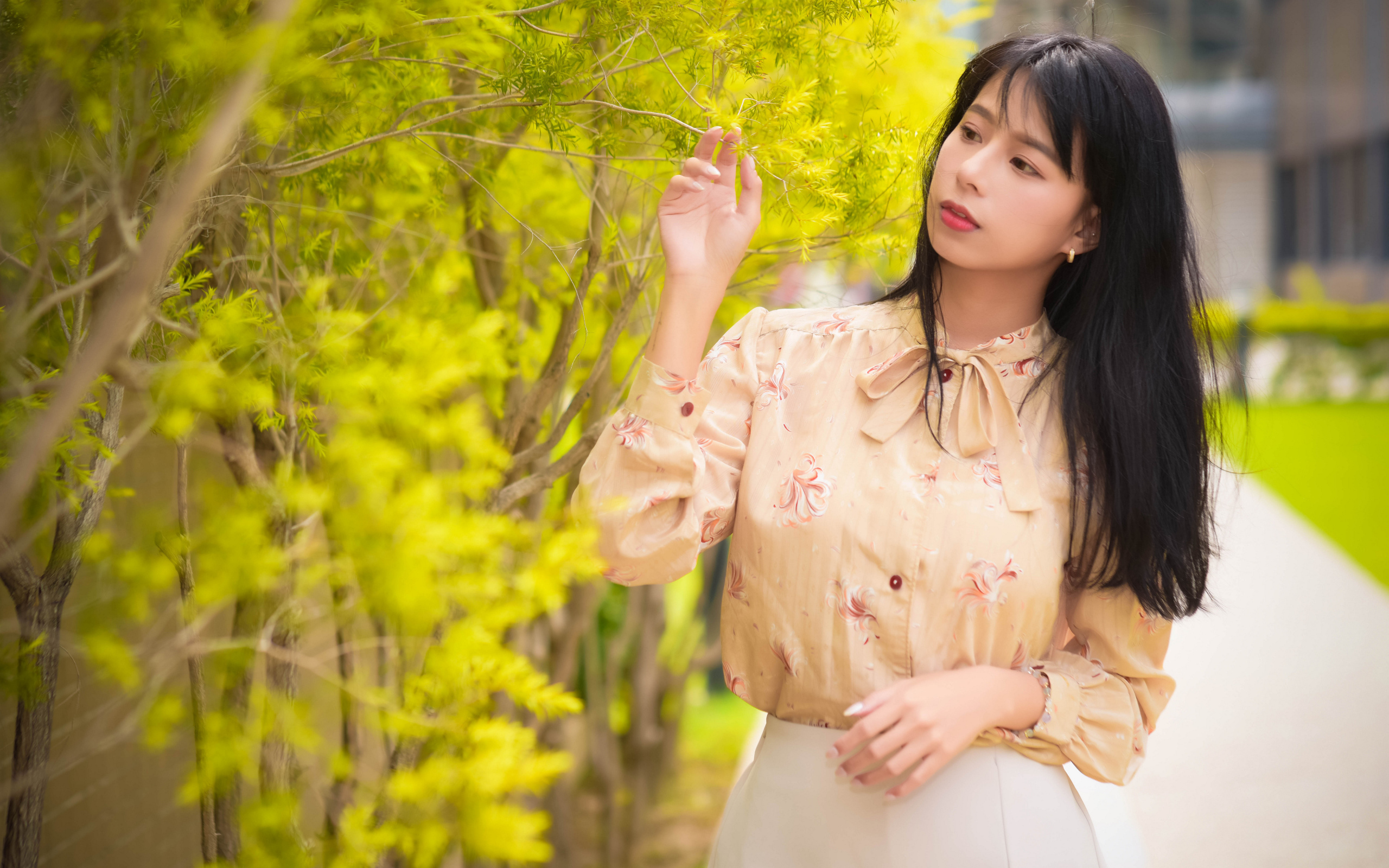 Молодая девушка азиатка стоит у дерева с зелеными листьями