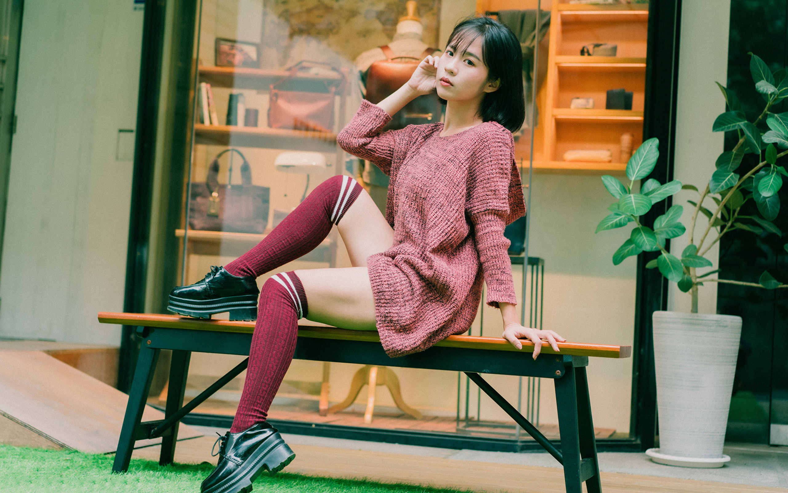 Девушка азиатка в теплом свитере сидит на лавке