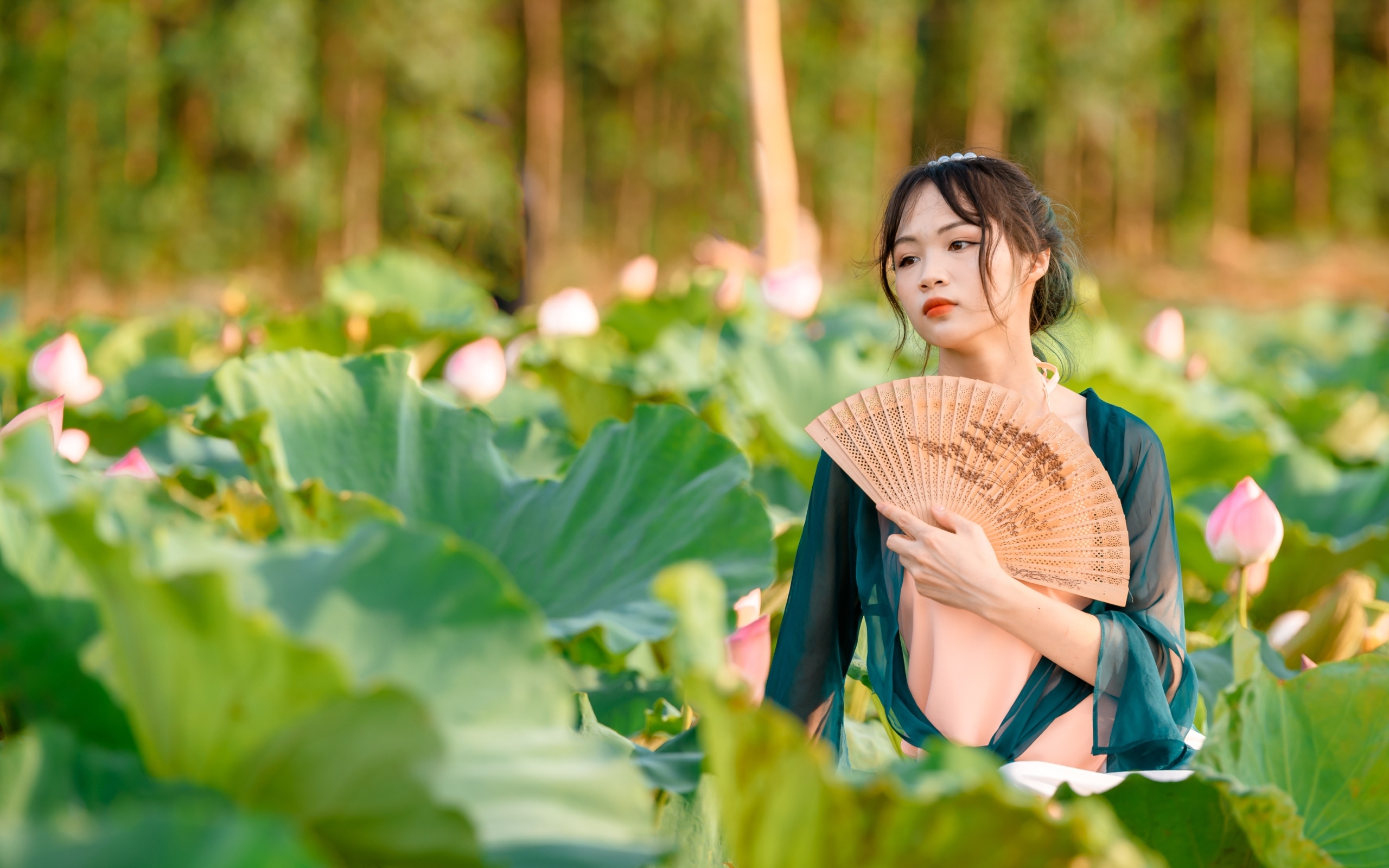 Девушка азиатка с веером в зеленых листьях лотоса