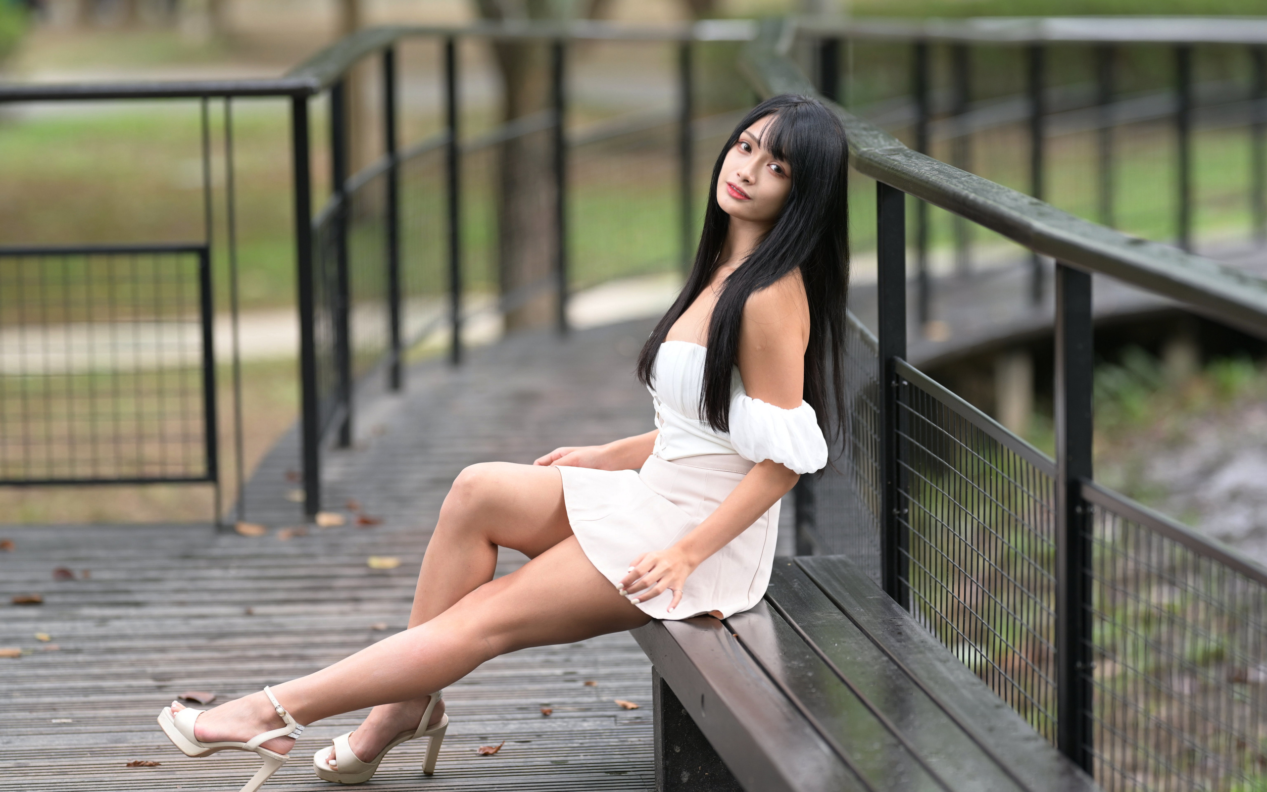 Красивая длинноволосая азиатка в белом платье сидит на лавке