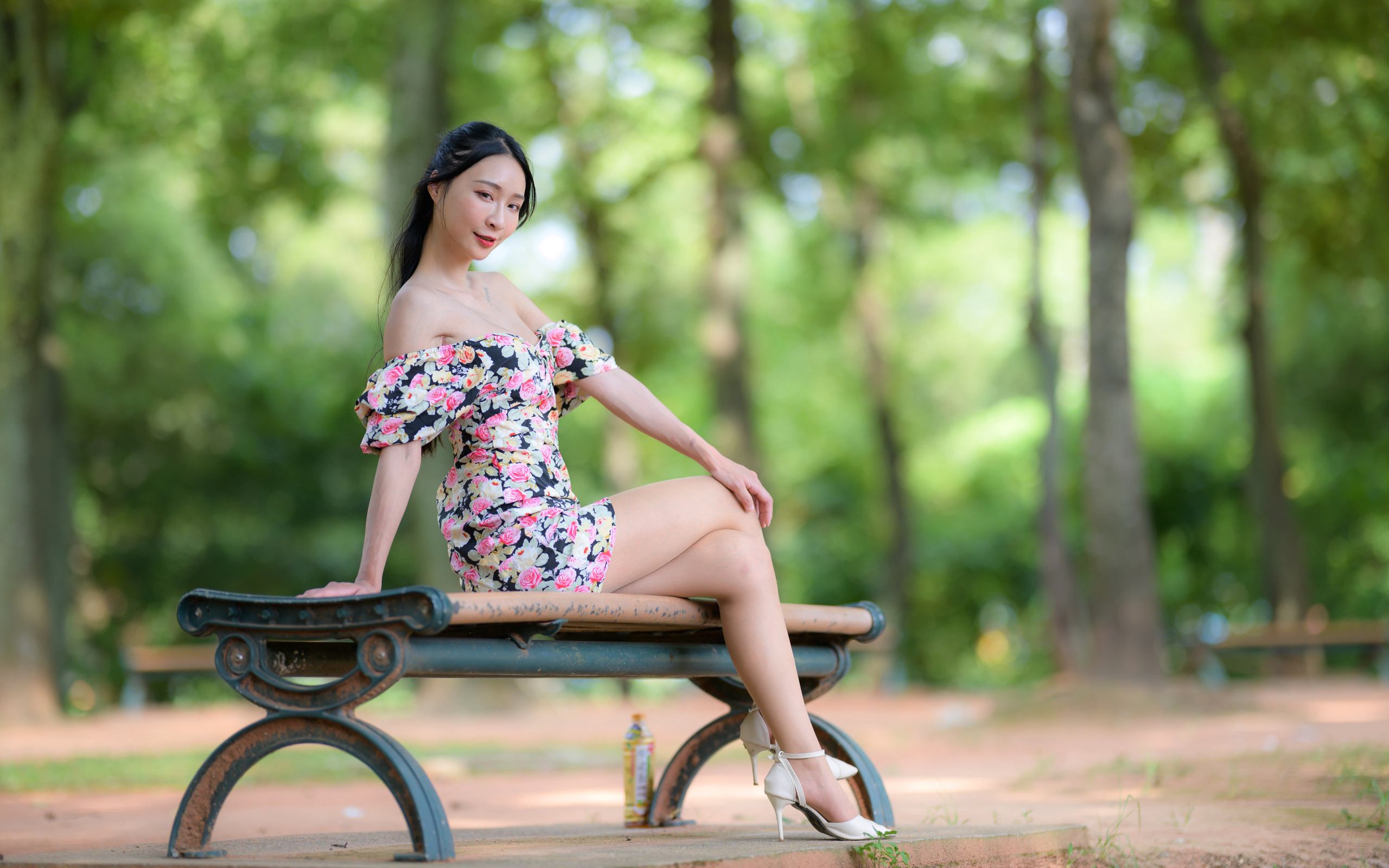 Милая девушка азиатка в платье сидит на лавке в парке