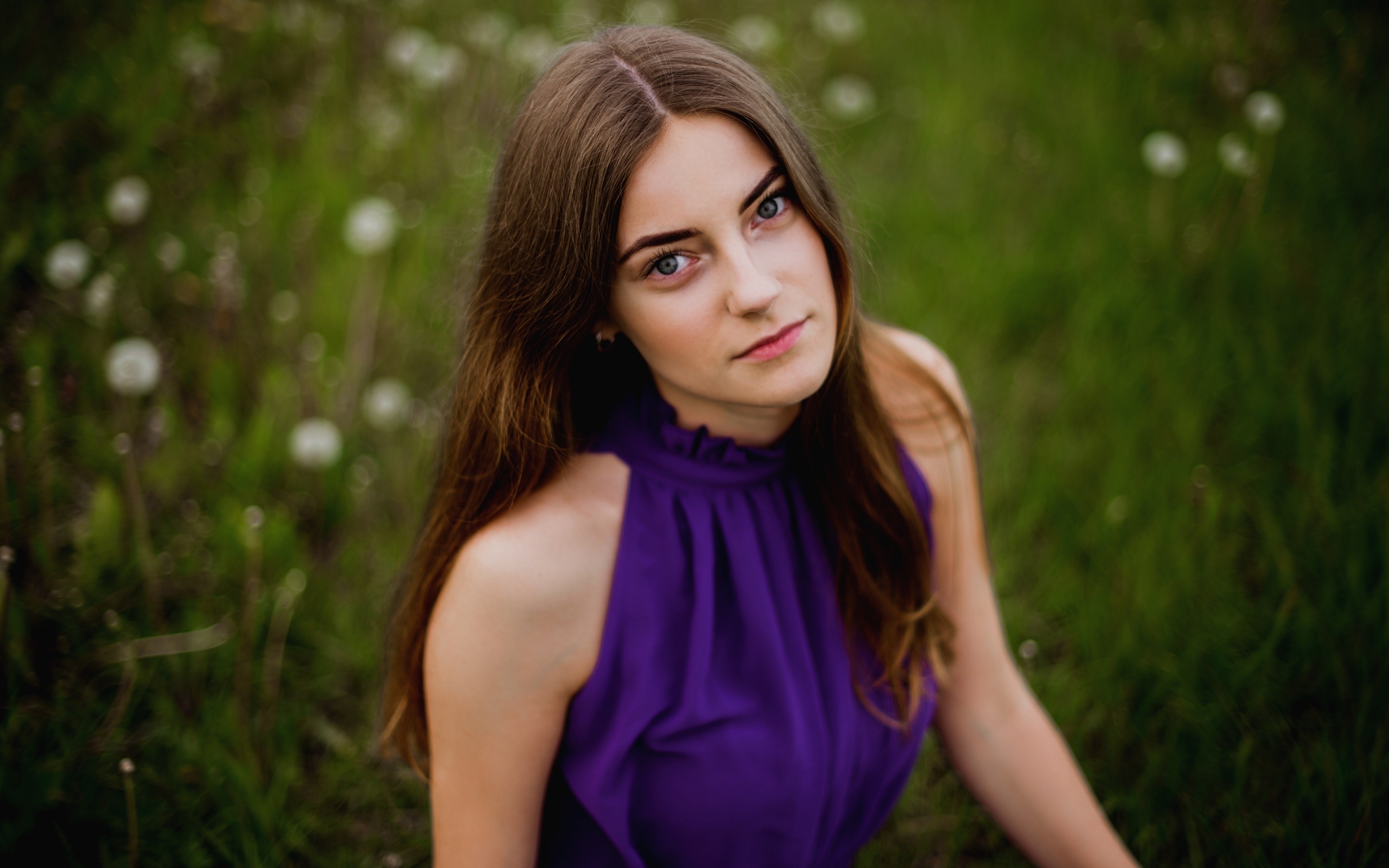 Милая девушка в фиолетовом платье сидит на траве