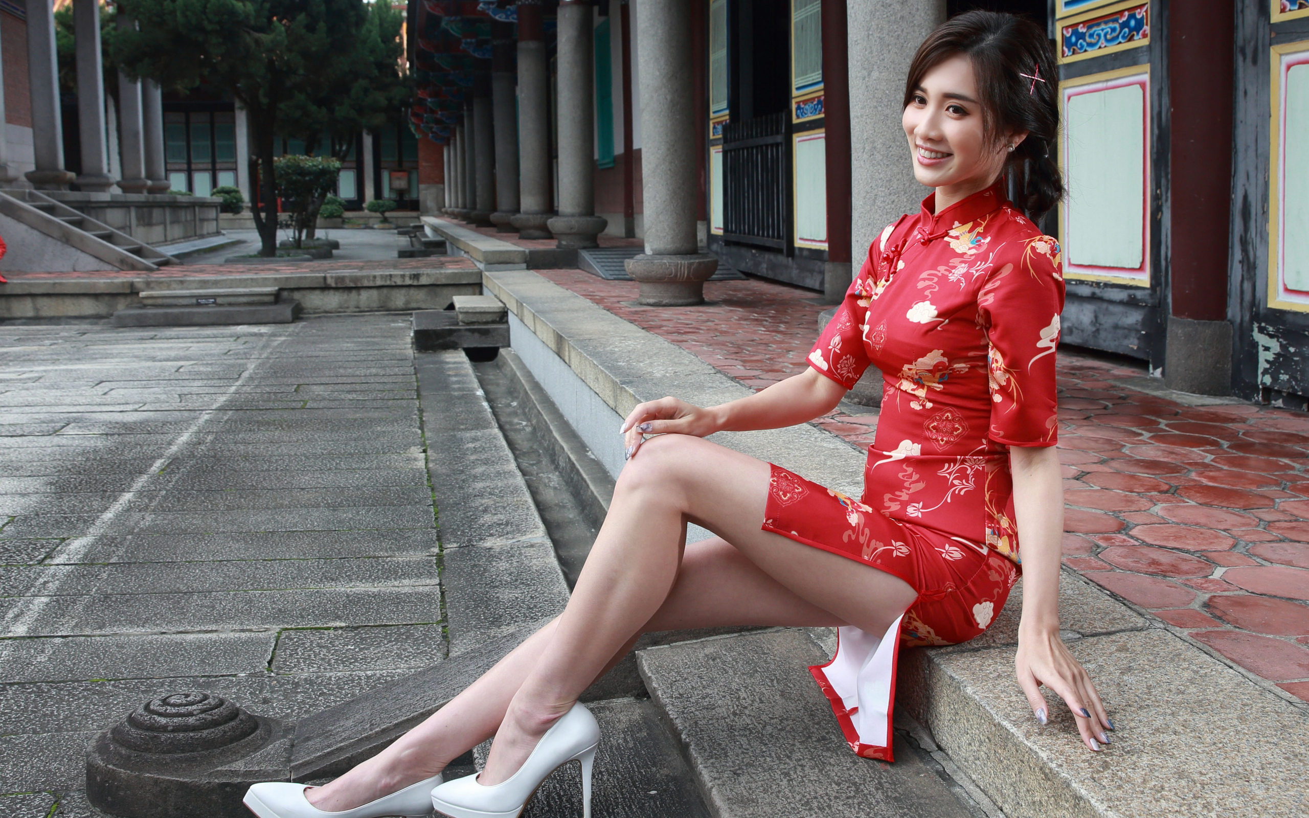 Улыбающаяся девушка азиатка в красном платье сидит на ступеньках