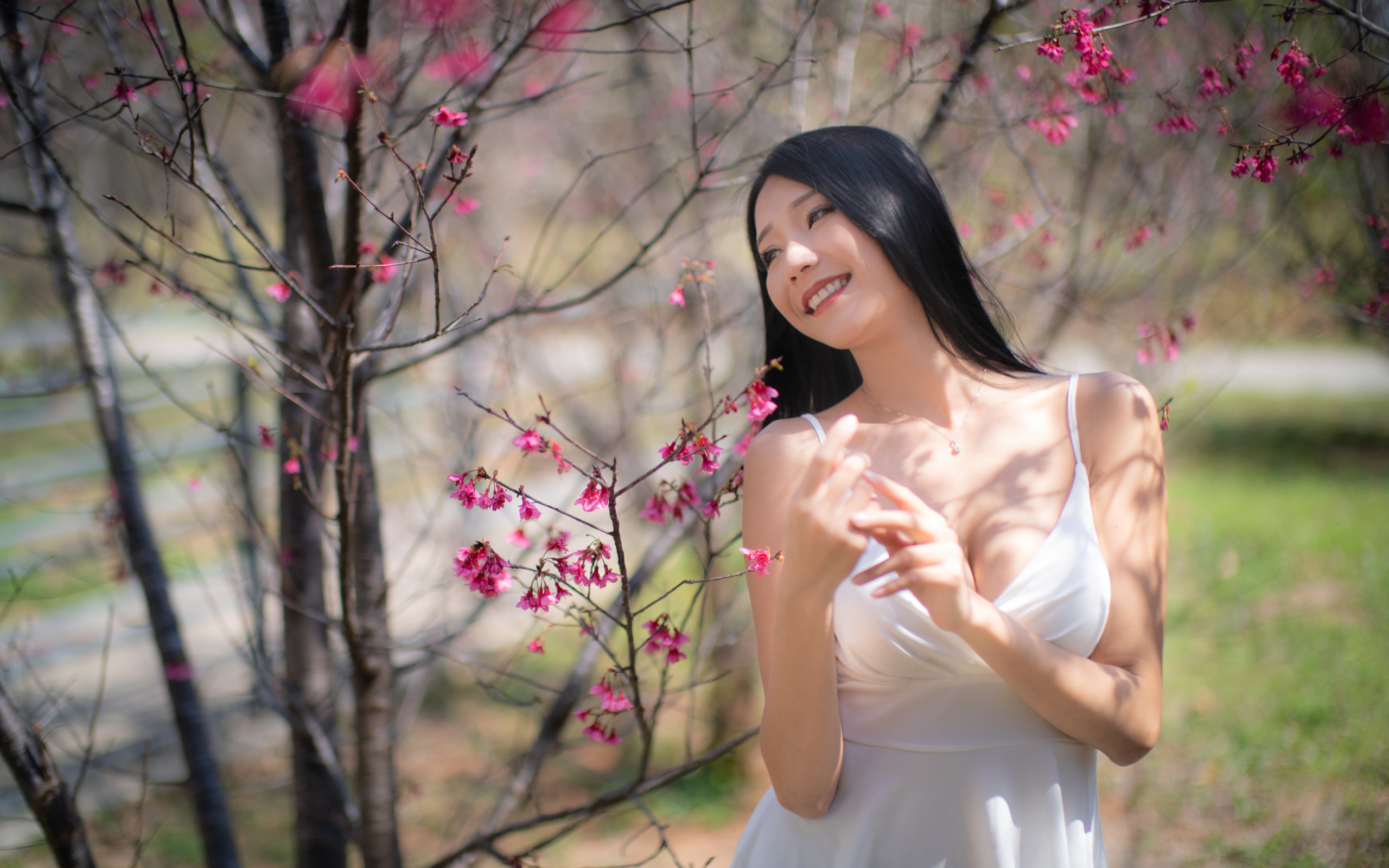 Улыбающаяся девушка в белом платье у дерева с цветами