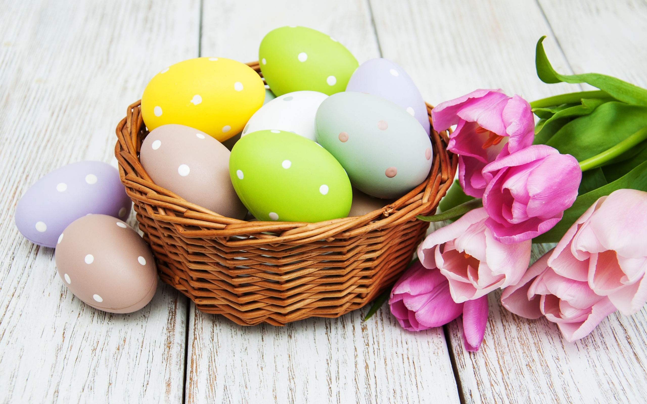 Корзина разноцветных яиц с тюльпанами на столе на Пасху