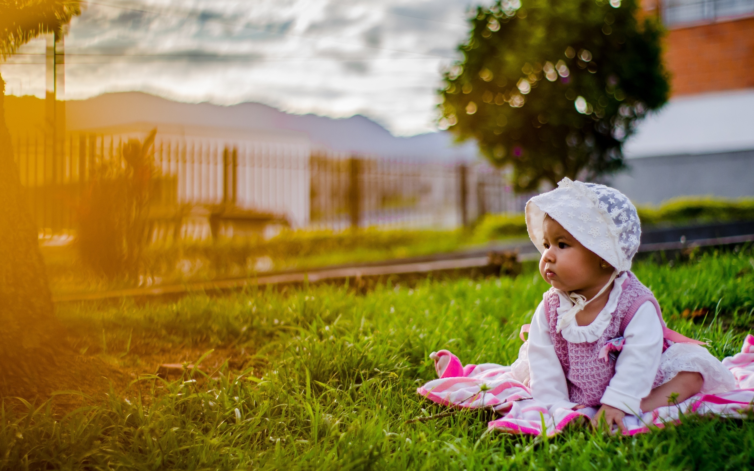 Маленькая девочка в розовом платье сидит на траве