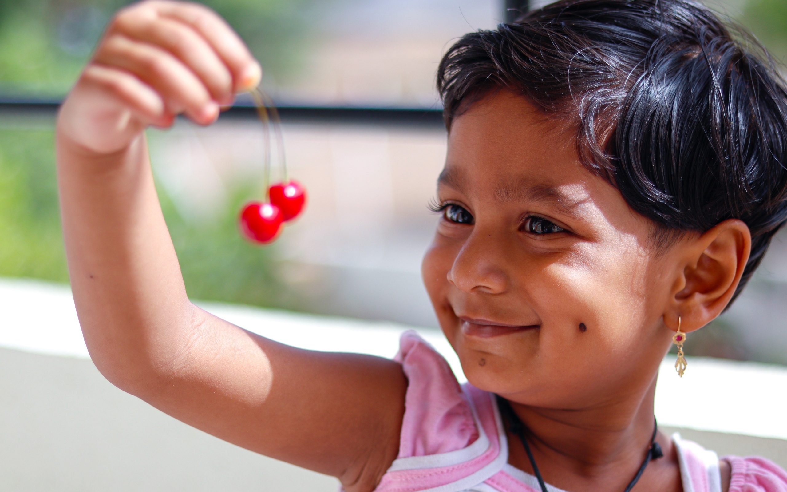 Маленькая улыбающаяся девочка с ягодами вишни в руках