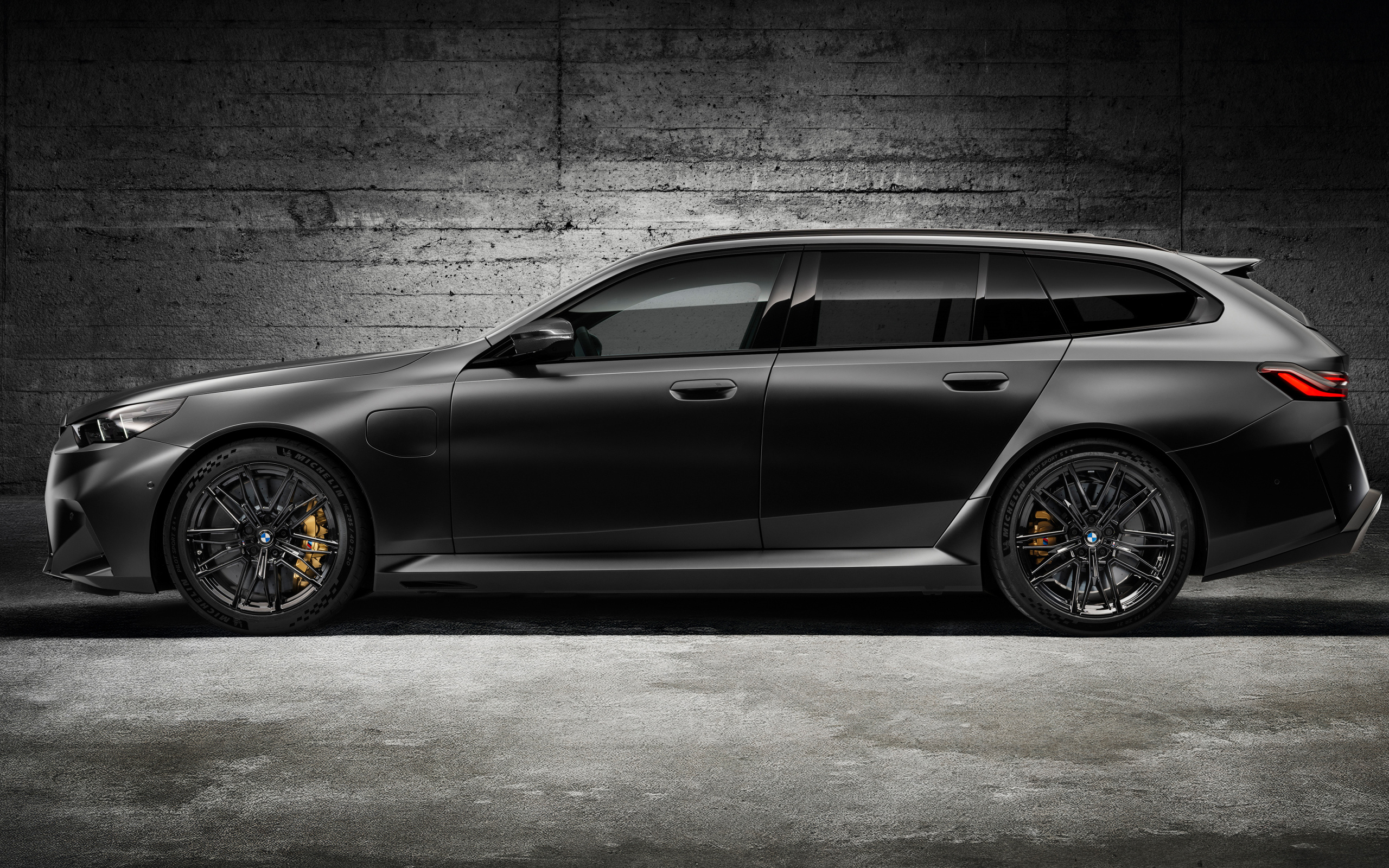 Вид сбоку на черный автомобиль BMW M5 Touring 2024 года