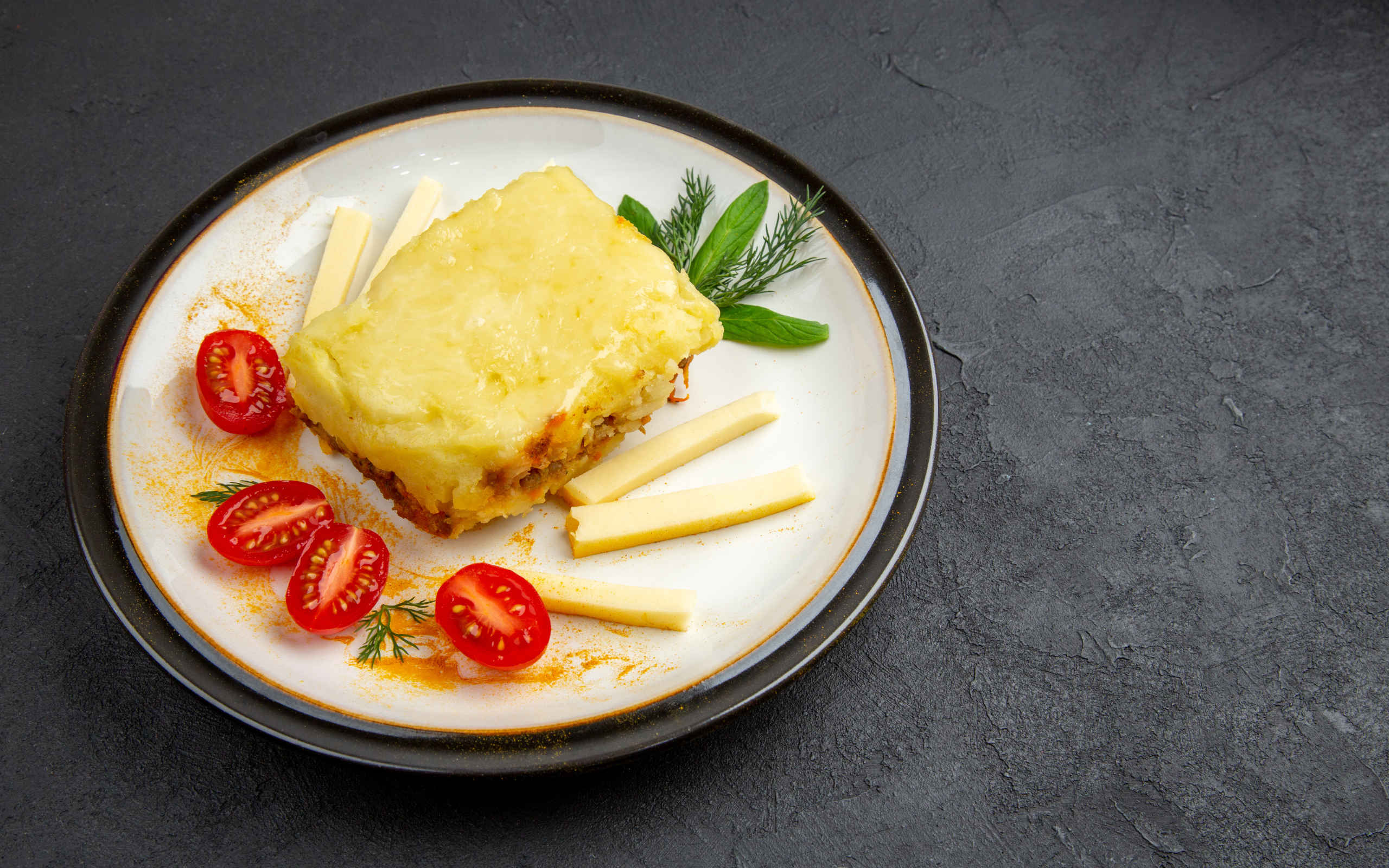 Кусок картофельной запеканки на тарелке с помидорами