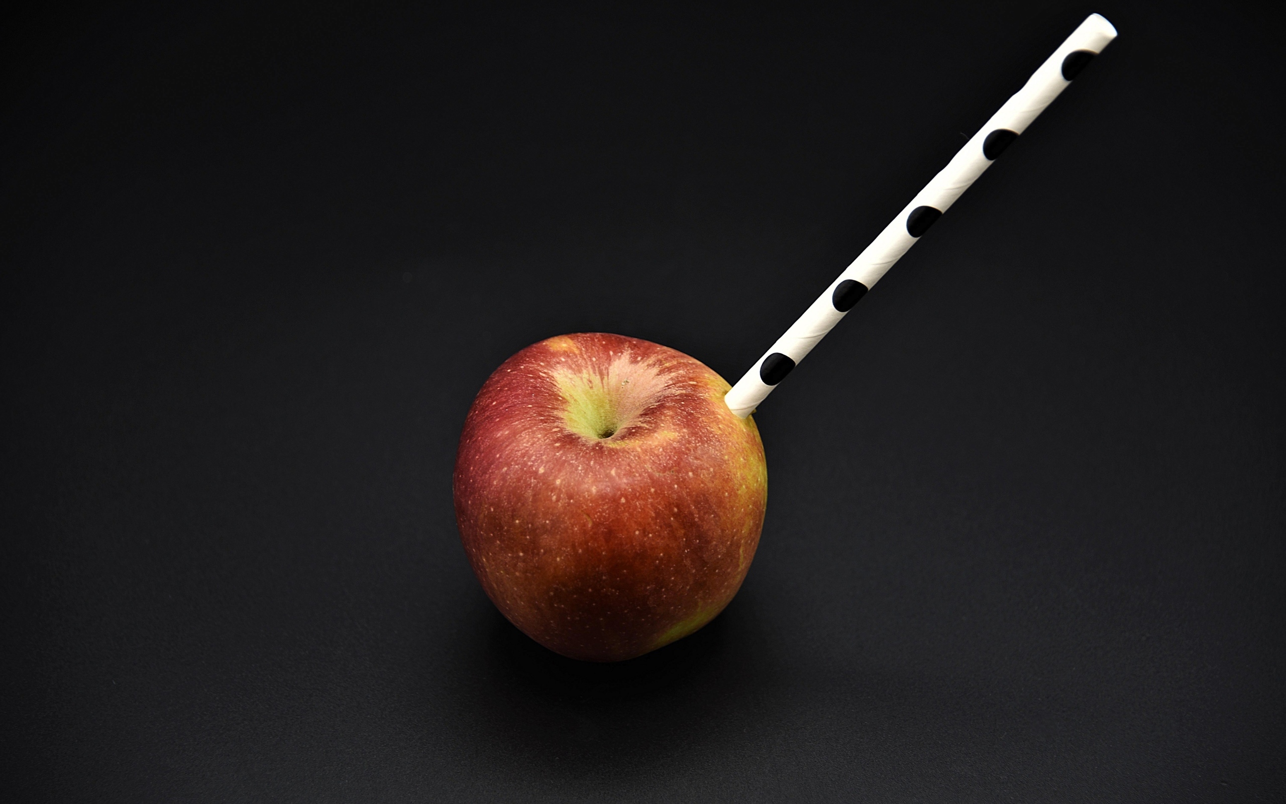 Большое красное яблоко с трубочкой на черном фоне
