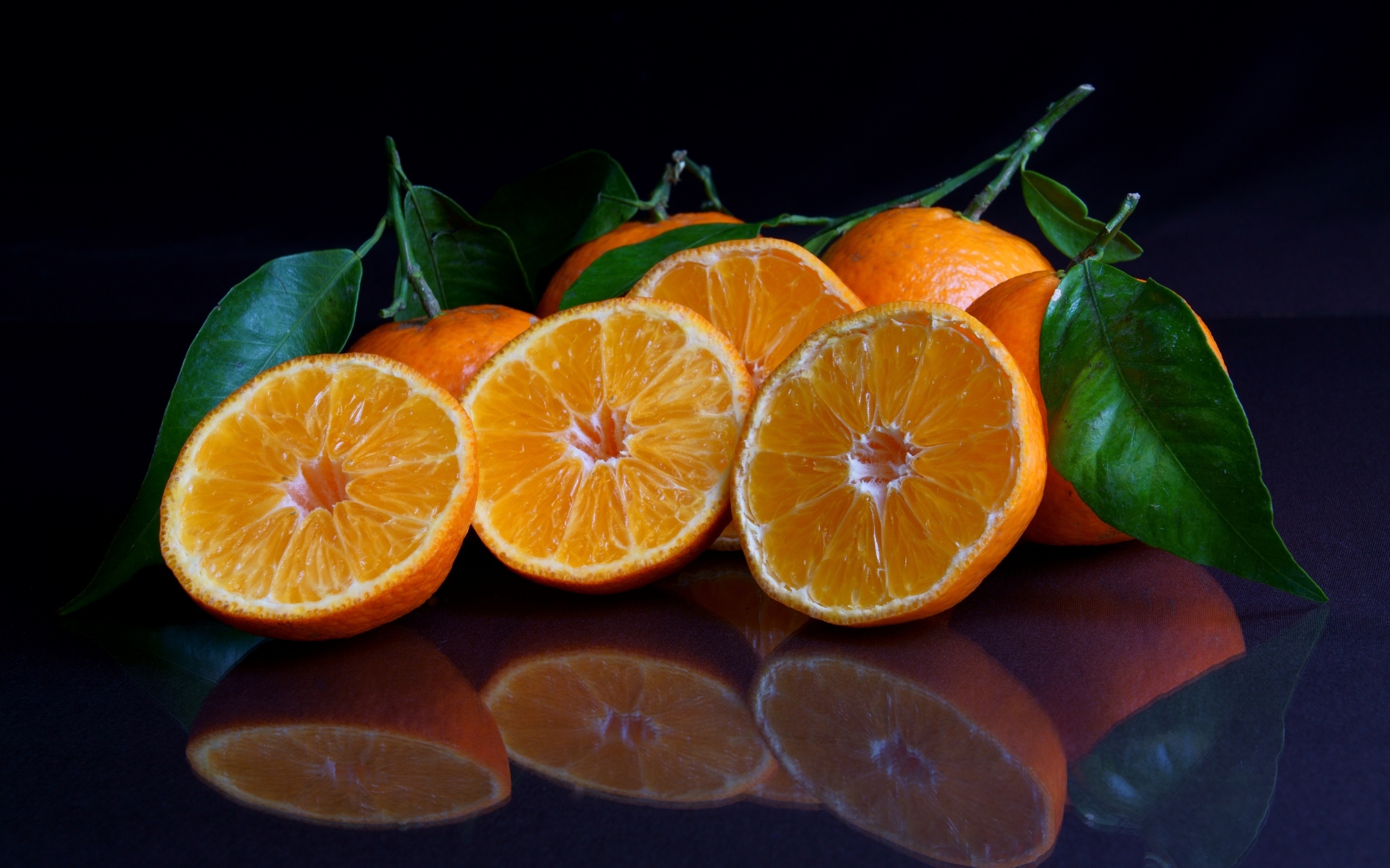 Половинки мандарина с листьями на черной поверхности