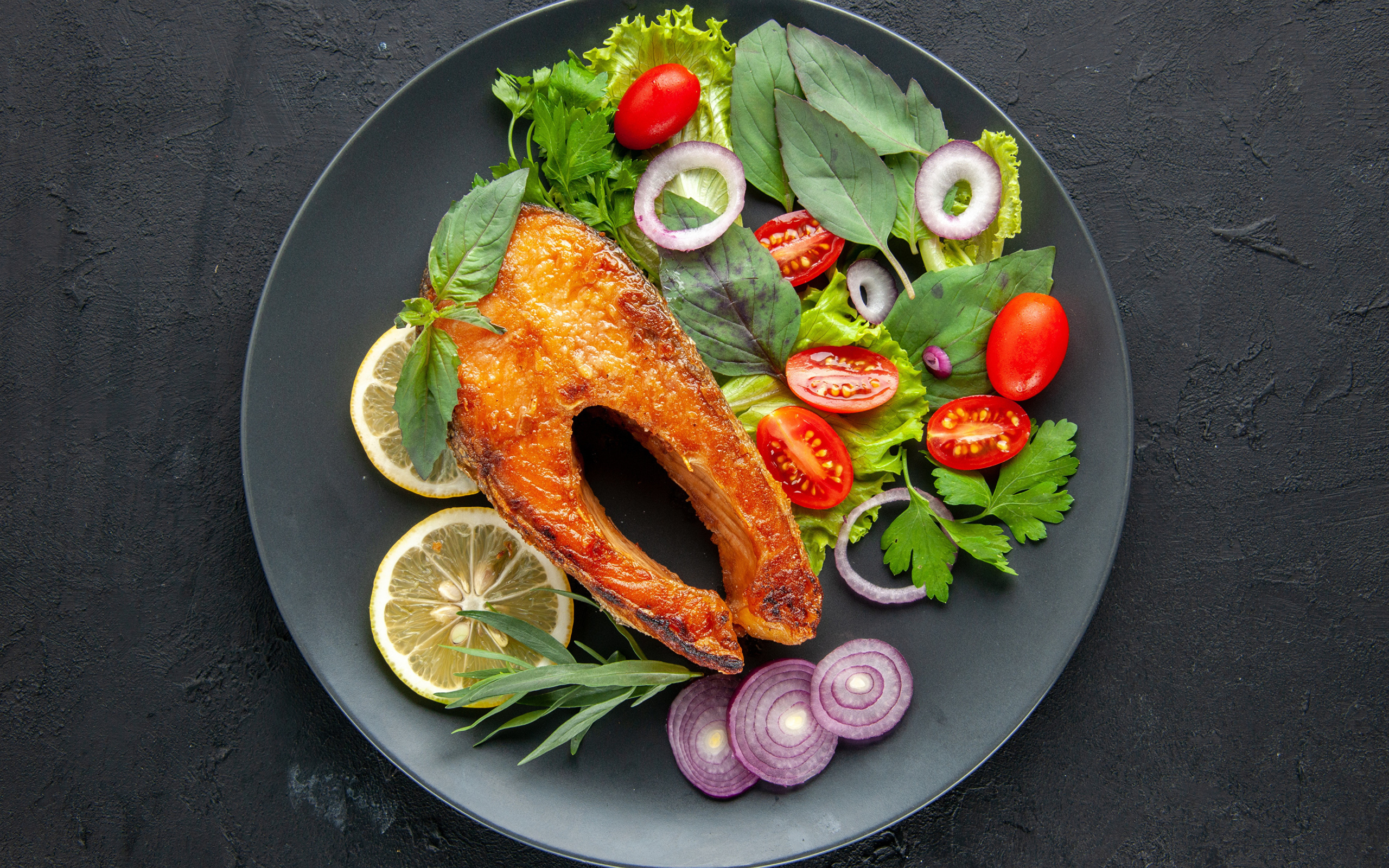 Жареная рыба на тарелке с зеленью,  лимоном и помидорами