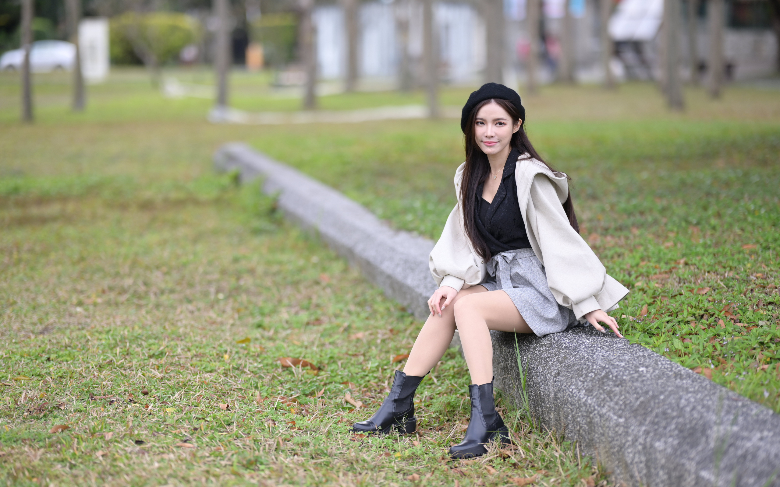 Девушка в пальто сидит на земле в парке