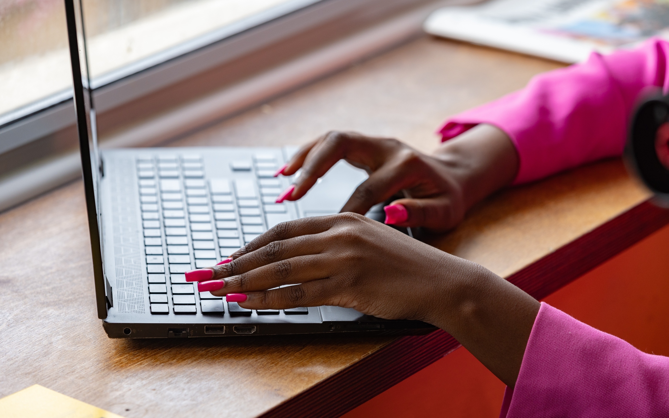 Девушка с розовым маникюром сидит за ноутбуком