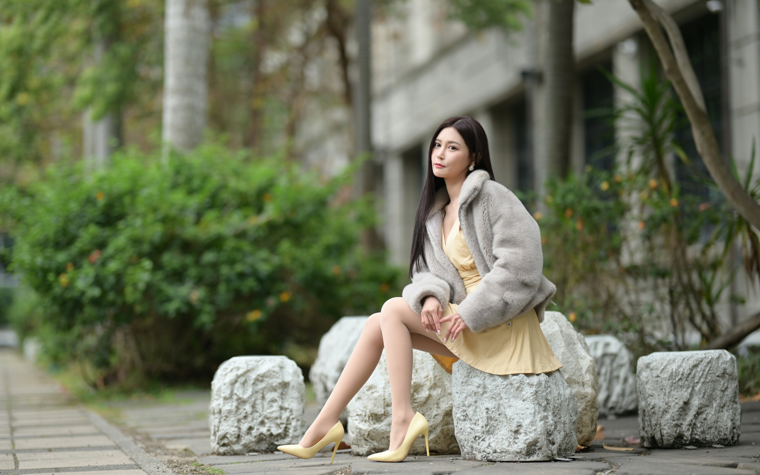 Азиатка в шубе сидит на квадратном камне