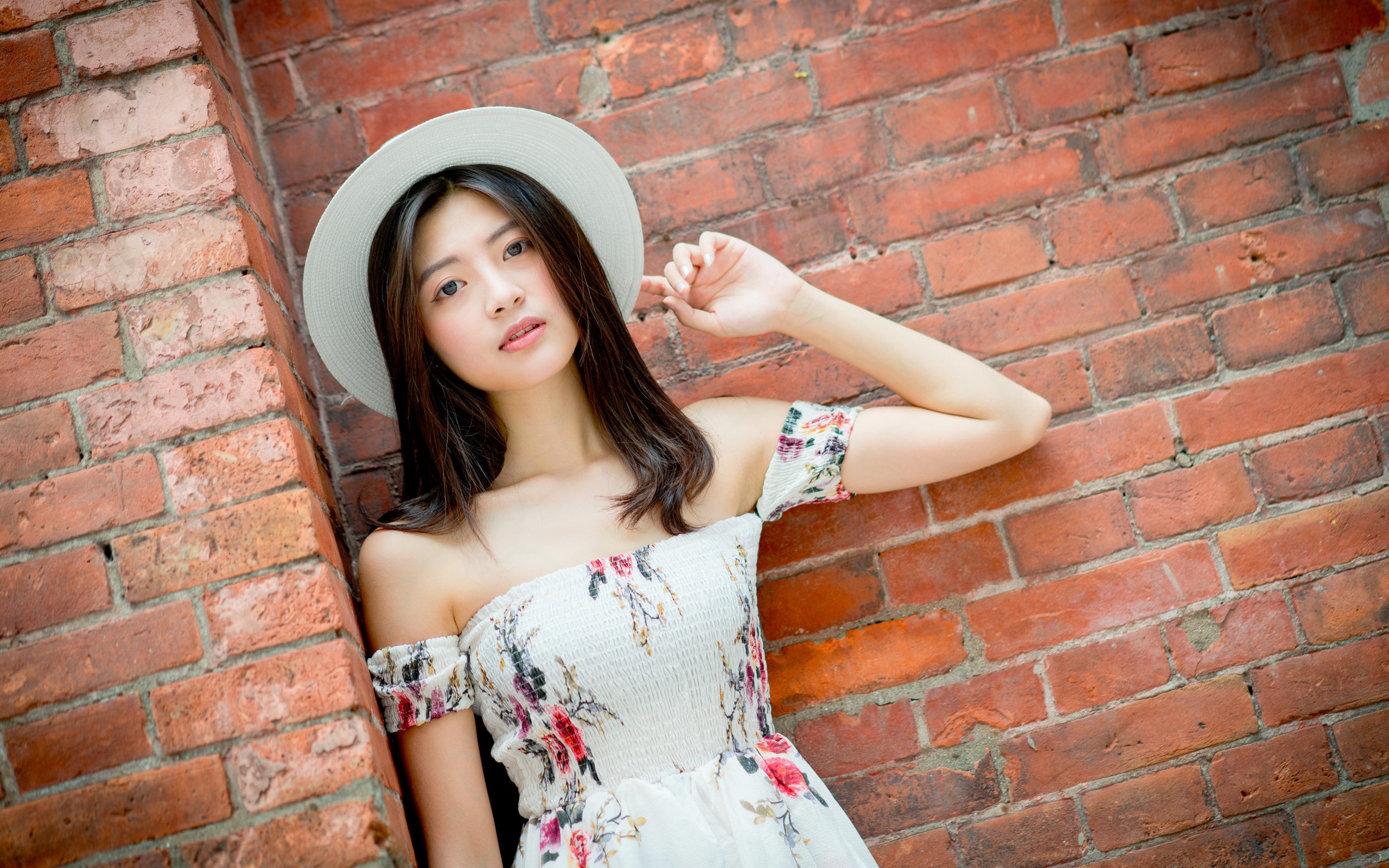 Азиатка в белой шляпе стоит у кирпичной стены