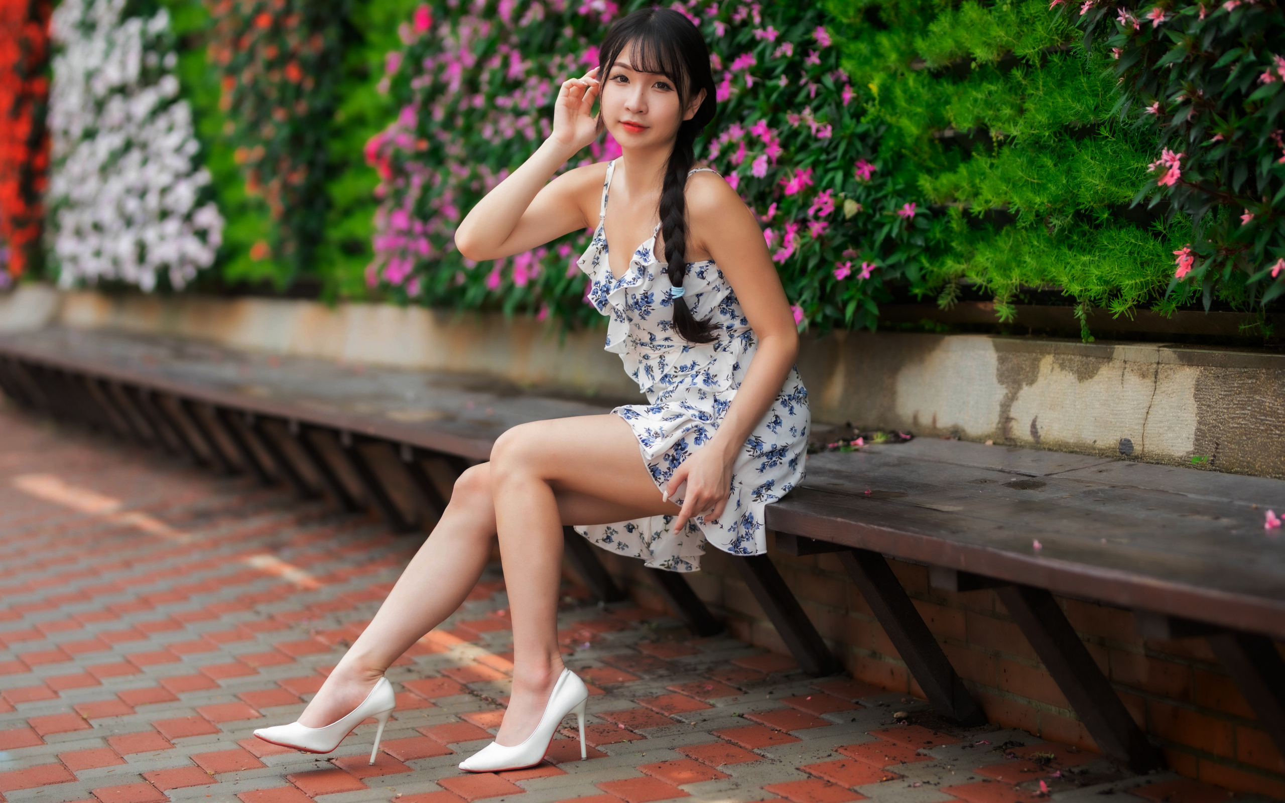 Азиатка в платье сидит на лавке у цветущих растений