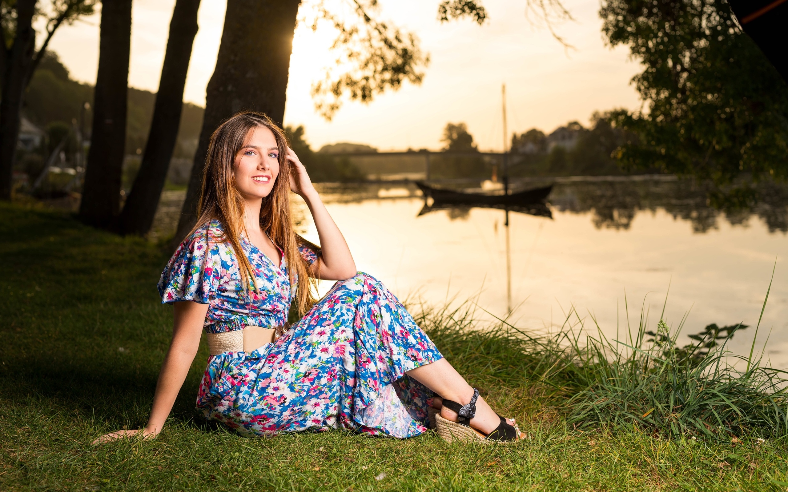 Милая девушка в платье сидит на берегу реки в парке