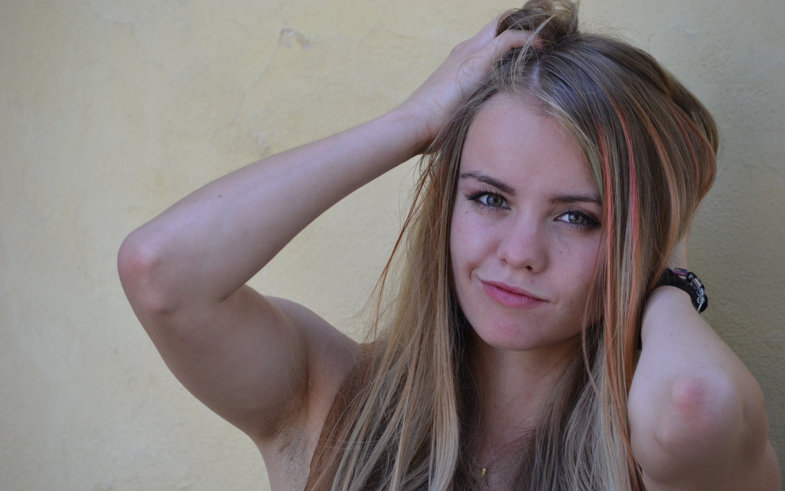 Девушка с руками в волосах у стены