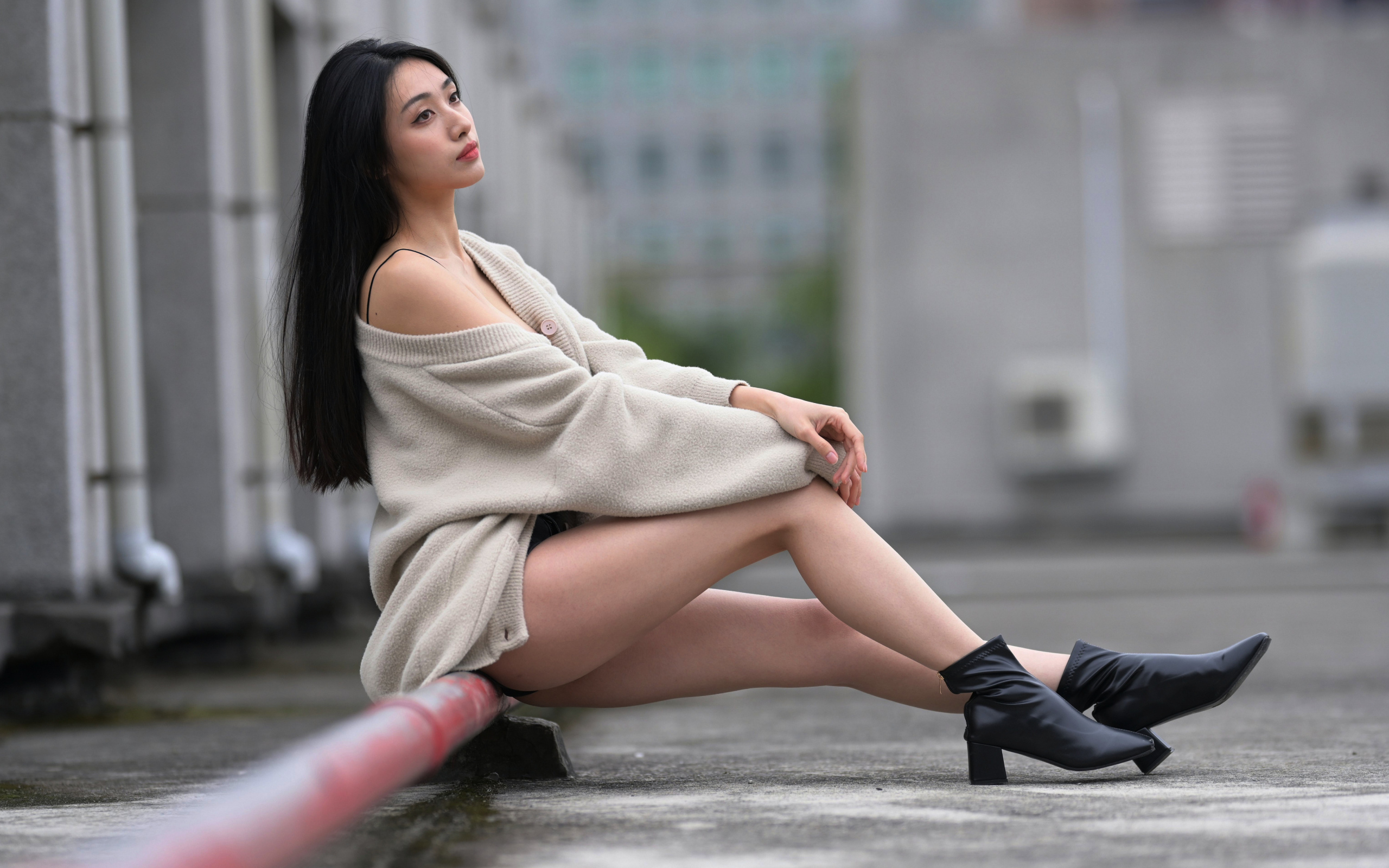 Грустная азиатка в теплой кофте сидит на трубе