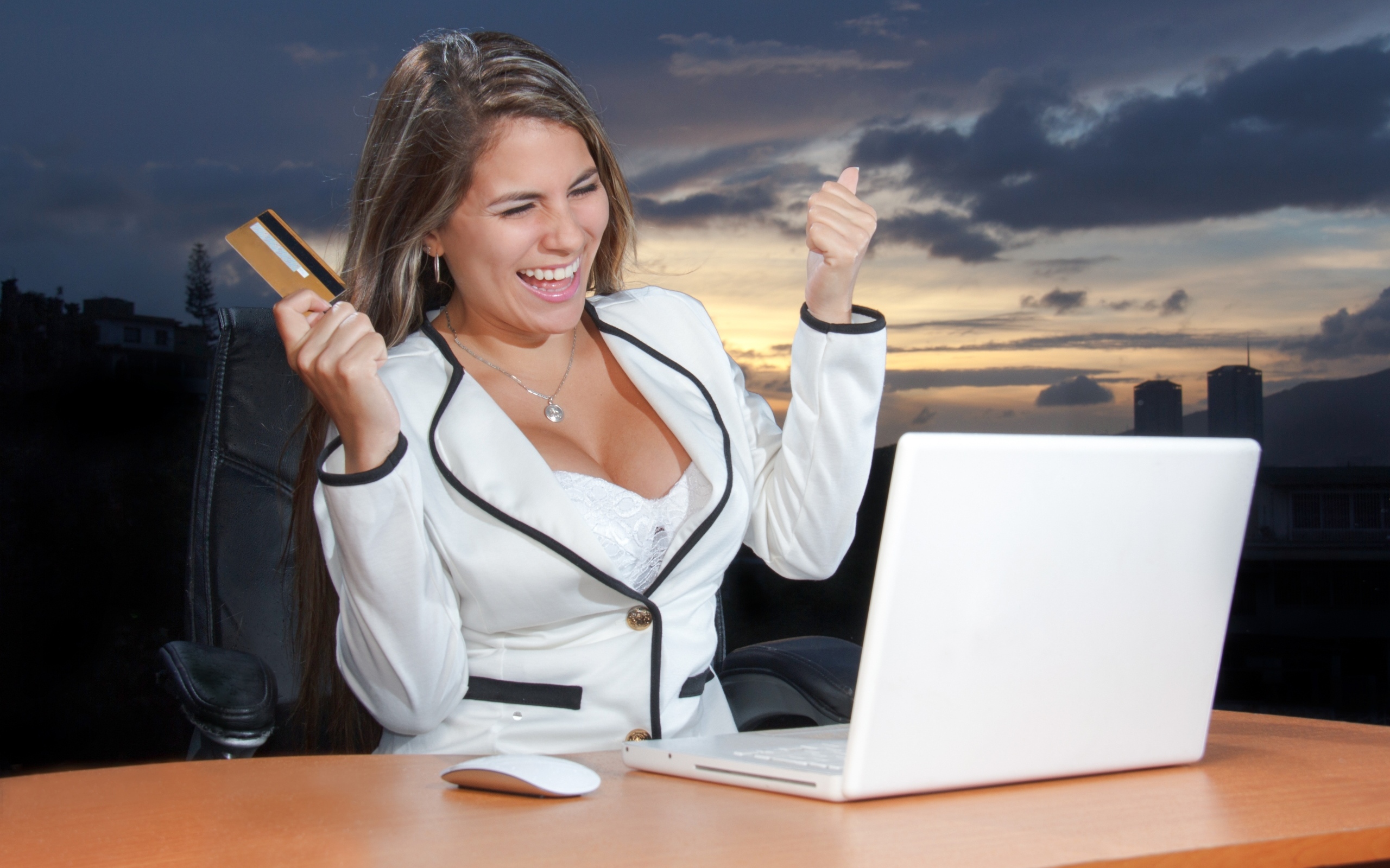 Довольная женщина с карточкой за столом с ноутбуком