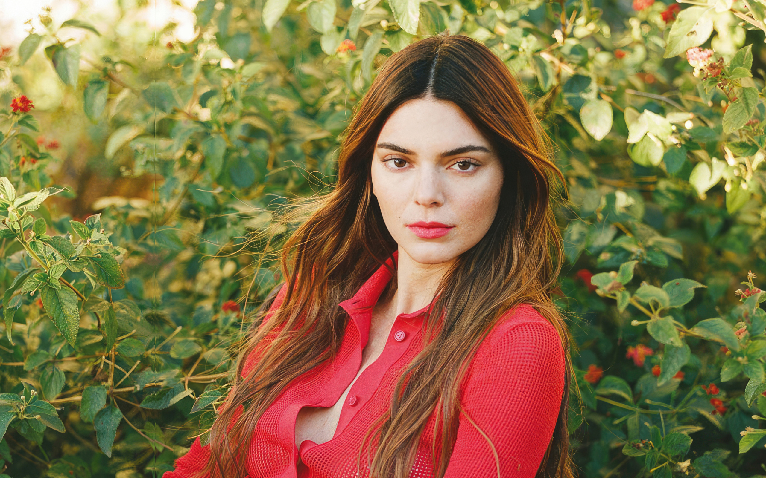 Американская модель Кендалл Дженнер в красной кофте стоит у куста