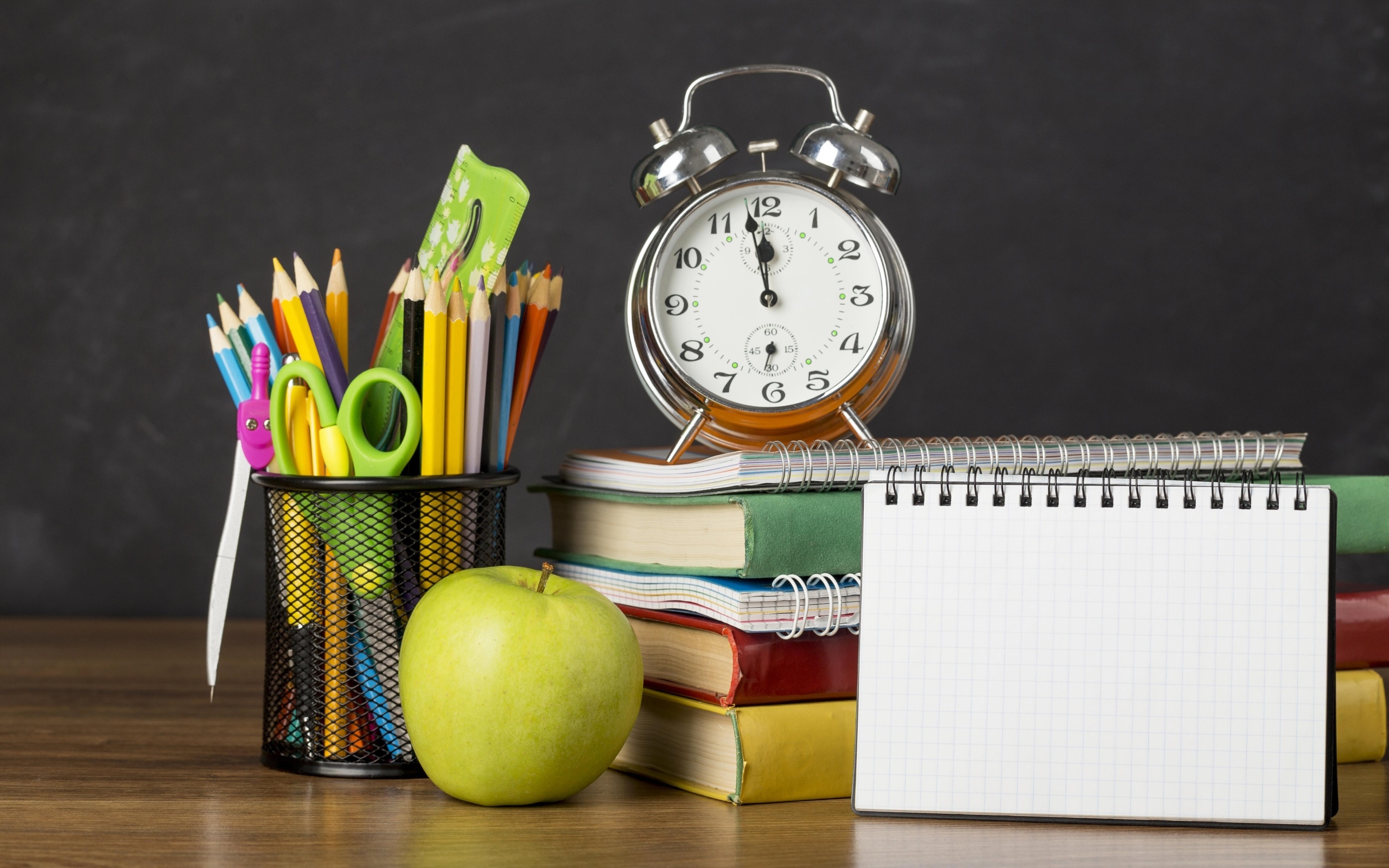 Канцелярские предметы на столе с будильником и книгами 