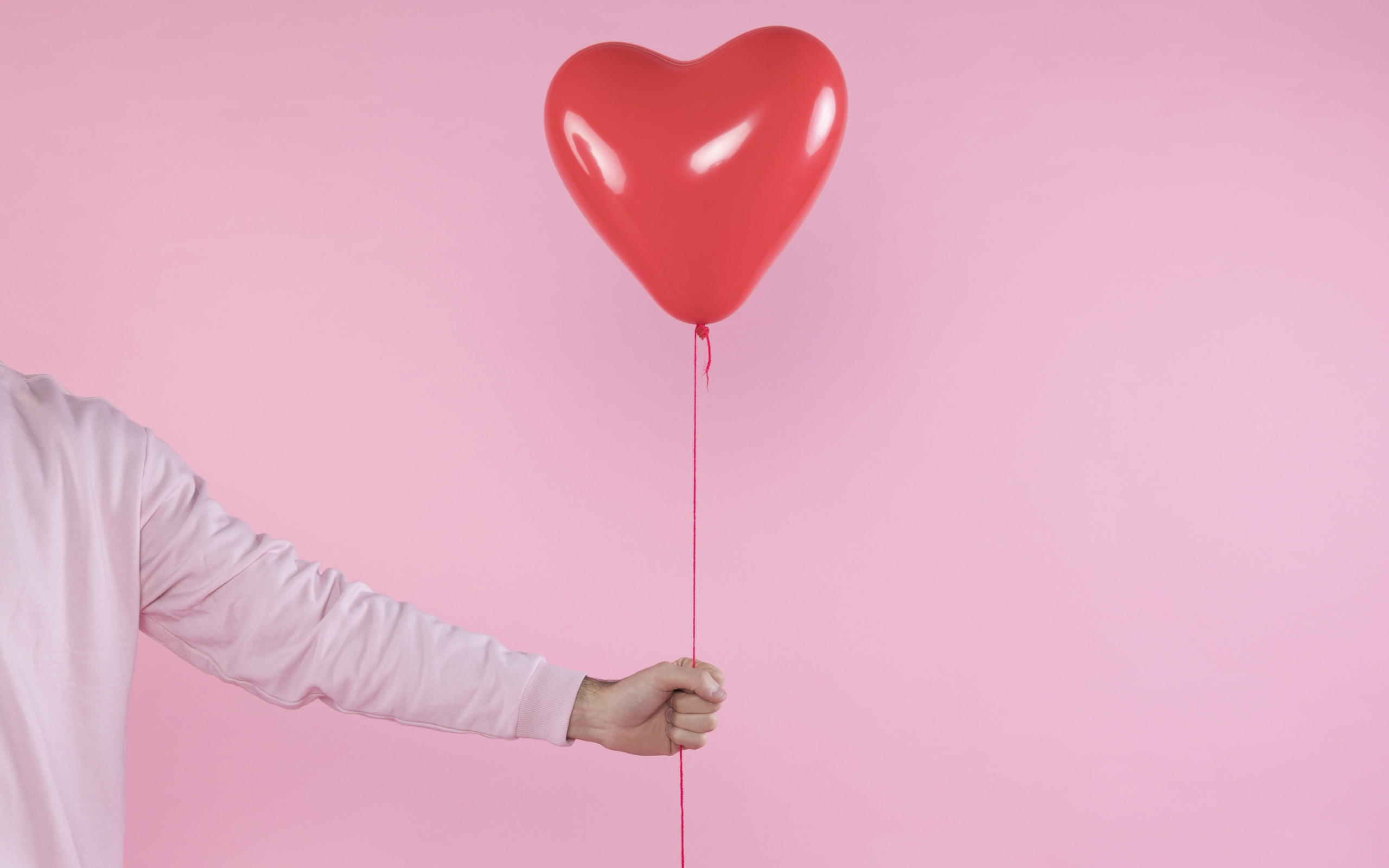 Шарик в форме сердца в руке на розовом фоне