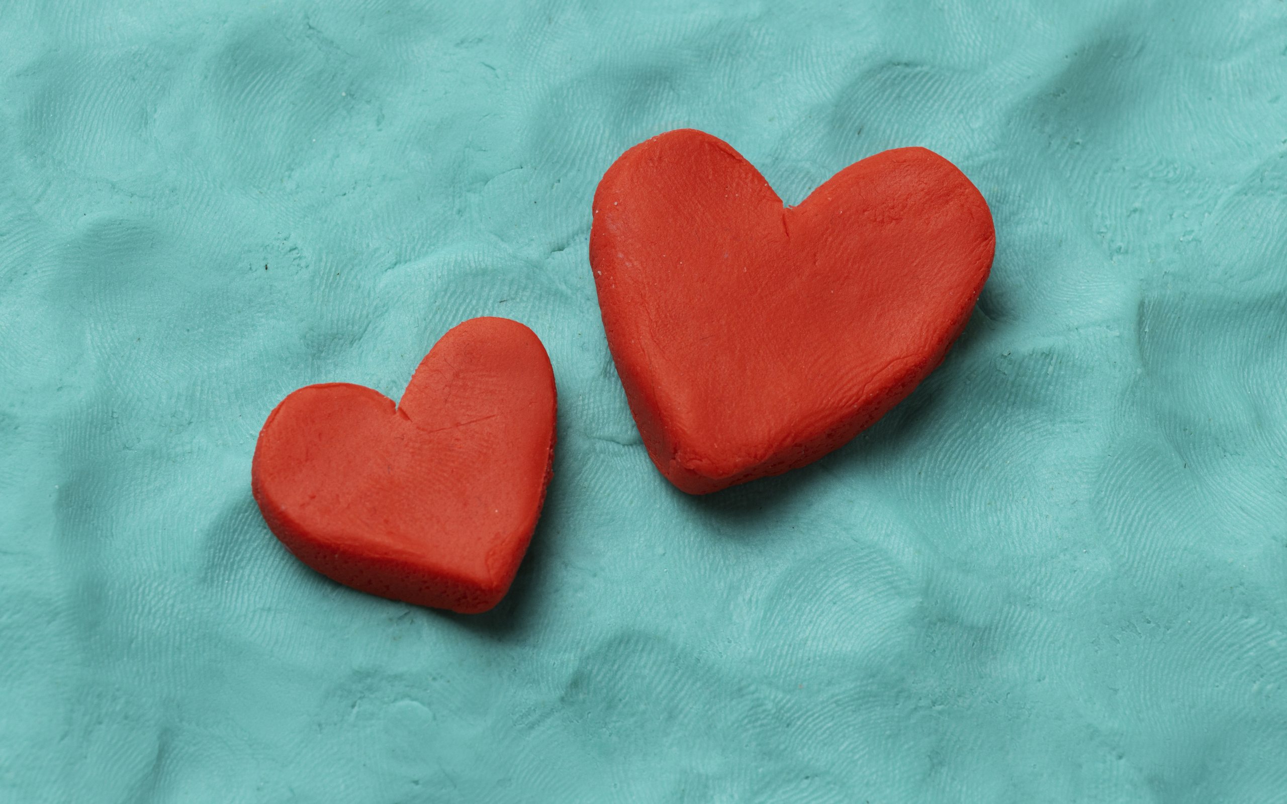 Два красных сердца из пластилина на голубом фоне