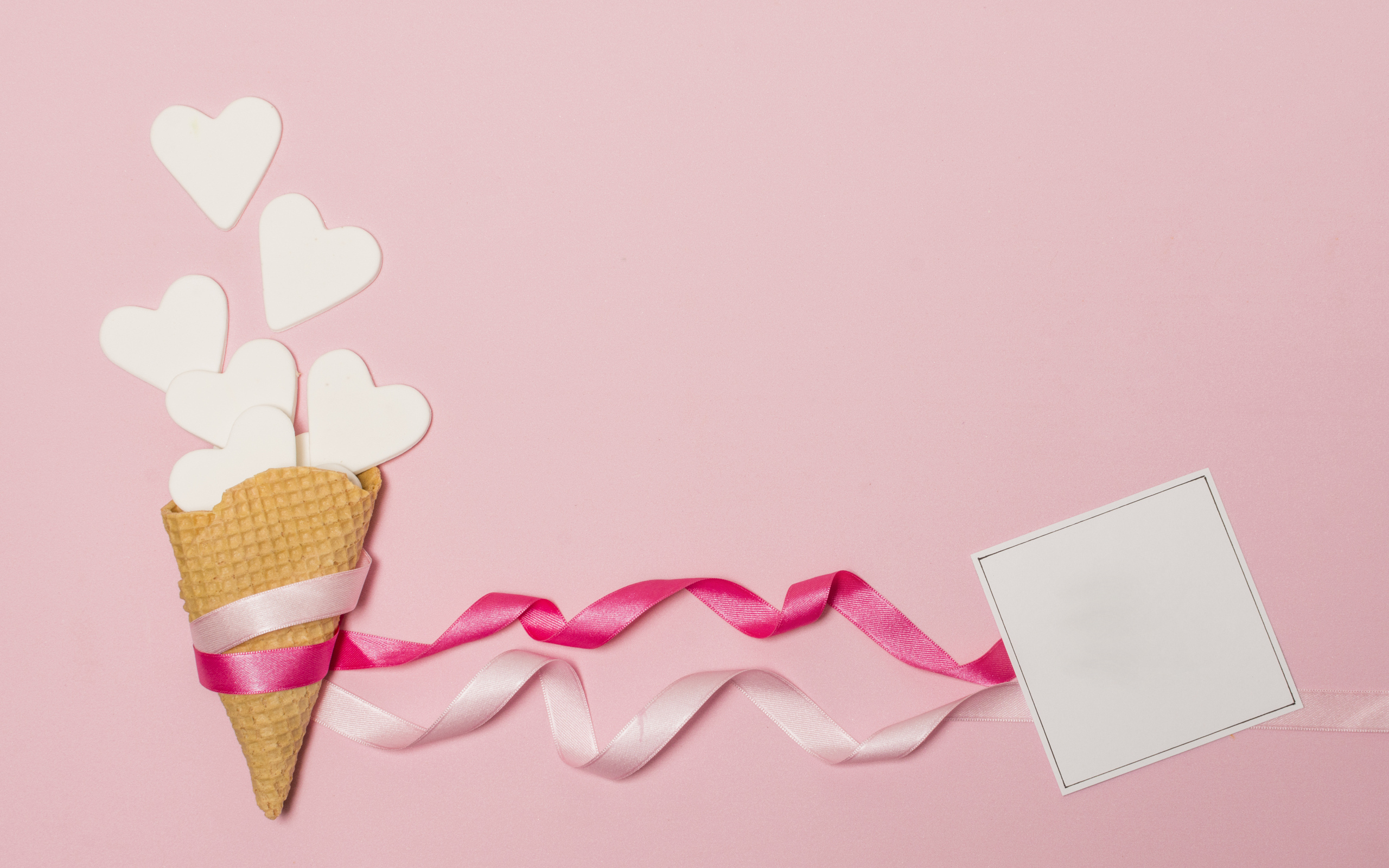 Вафельный рожок с сердечками, лентами и листом бумаги на розовом фоне