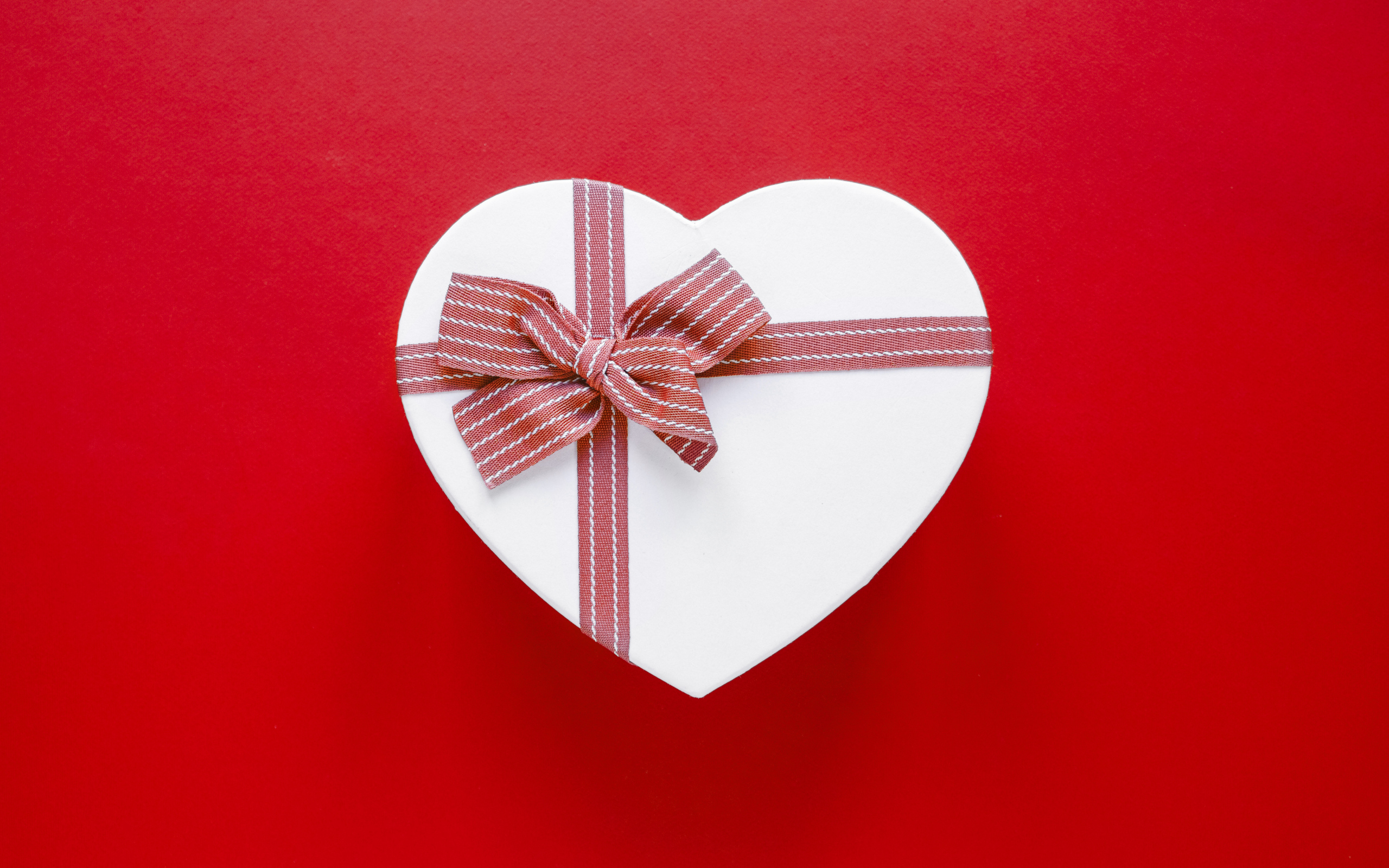 Белая коробка в форме сердца с бантом на красном фоне
