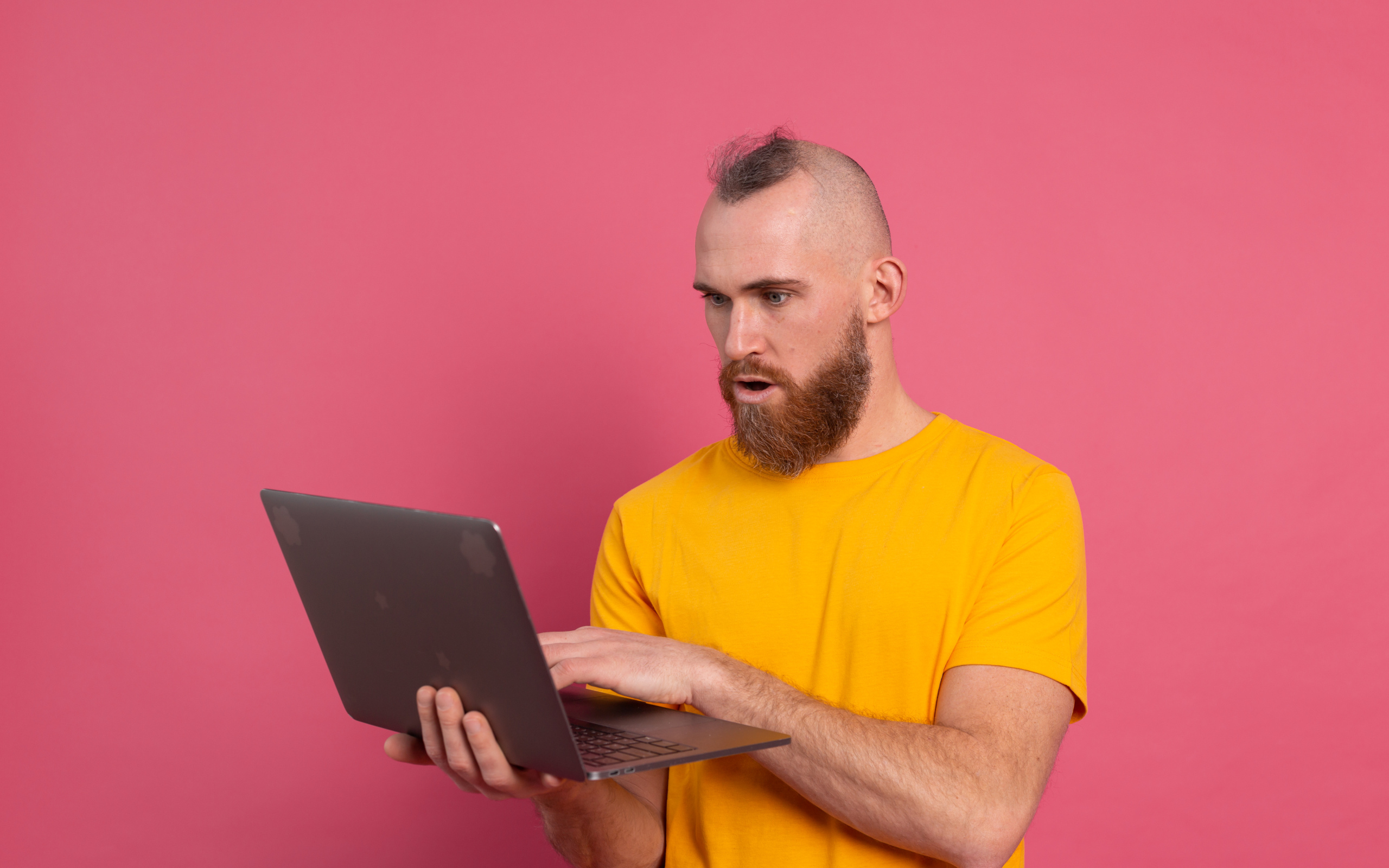 Удивленный мужчина с ноутбуком на розовом фоне