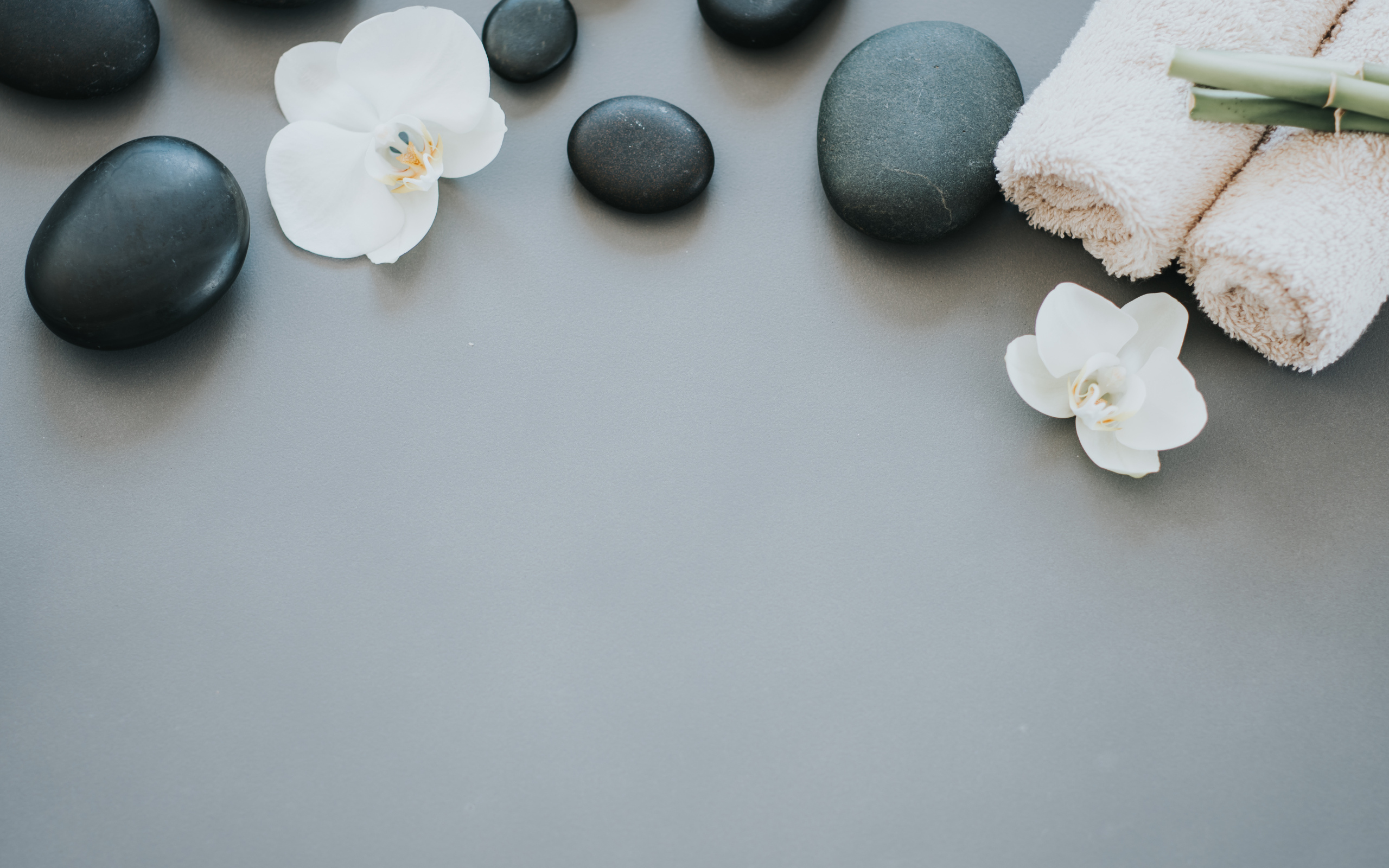 Черные камни с цветами орхидеи и полотенцем на сером фоне