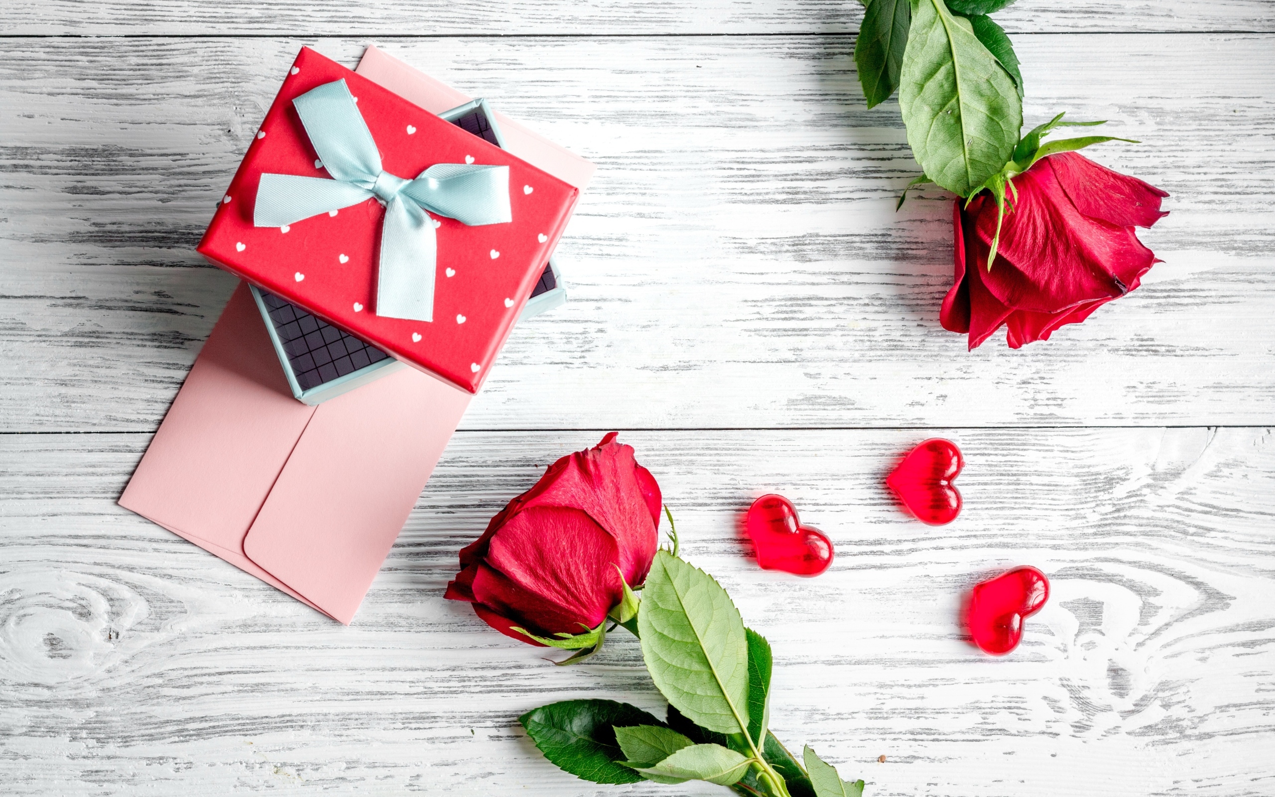 Две красные розы с подарком и сердечками на столе
